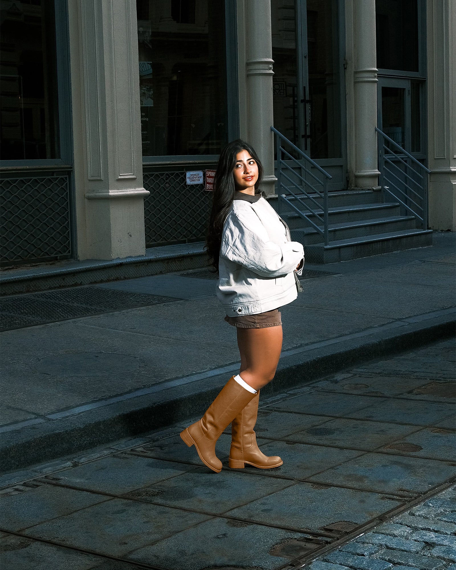 Brown knee high boots styled with jeans, shown walking on pavement