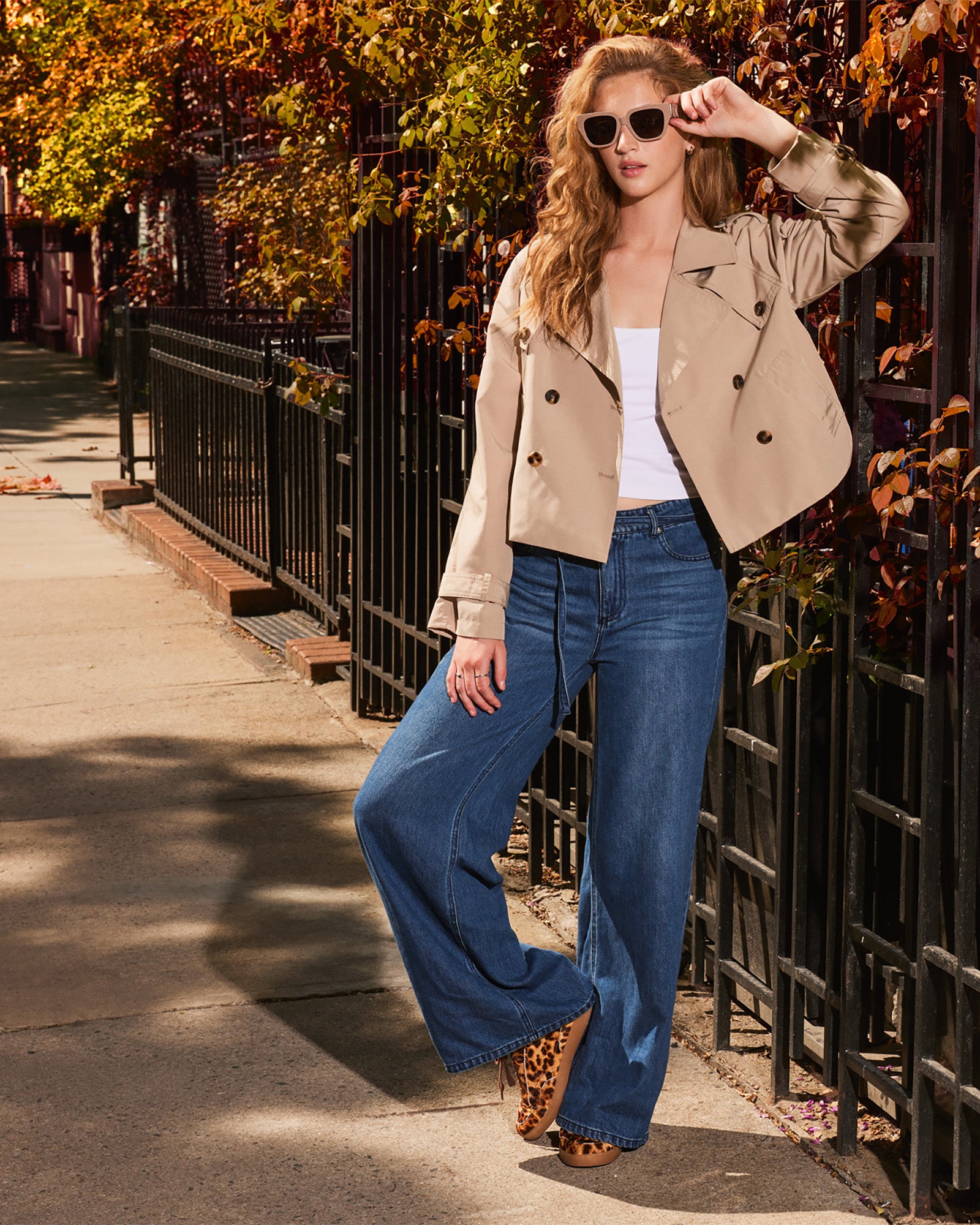 Front view of khaki cropped trench jacket on model in an urban setting.