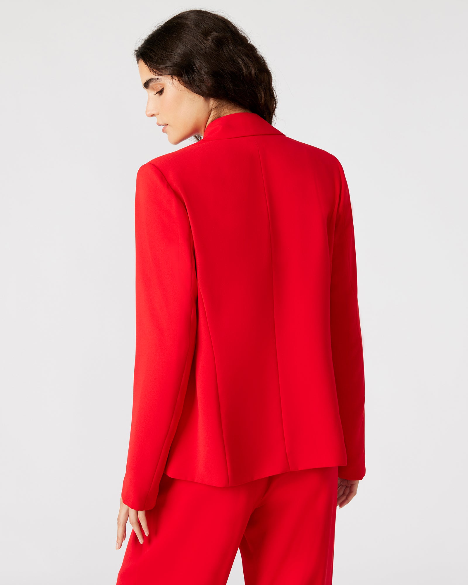 Model wearing red blazer dress outdoors with sunlight highlighting structured fit.
