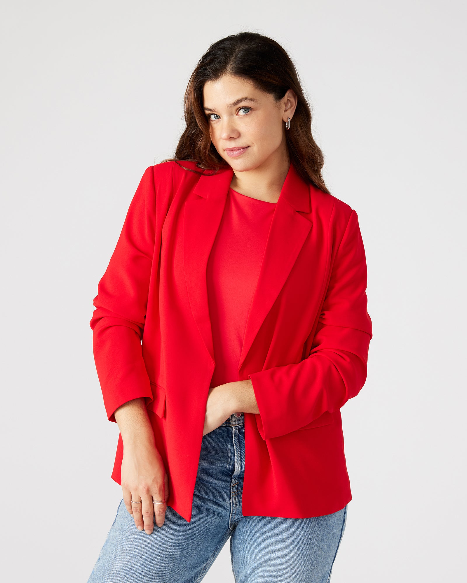 Model wearing red blazer dress outdoors with sunlight highlighting structured fit.