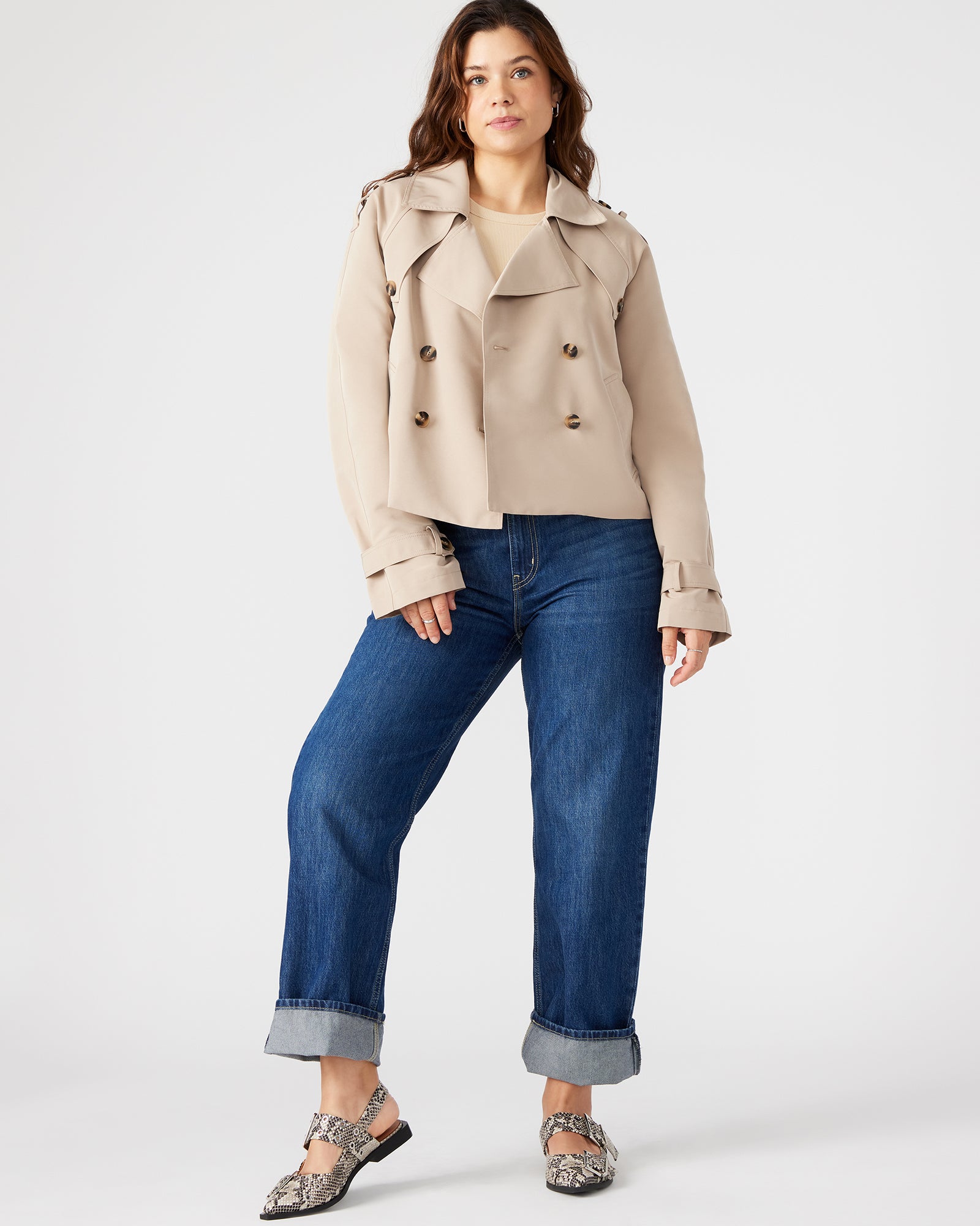 Close-up of double-breasted button closure and side pockets of cropped trench jacket.