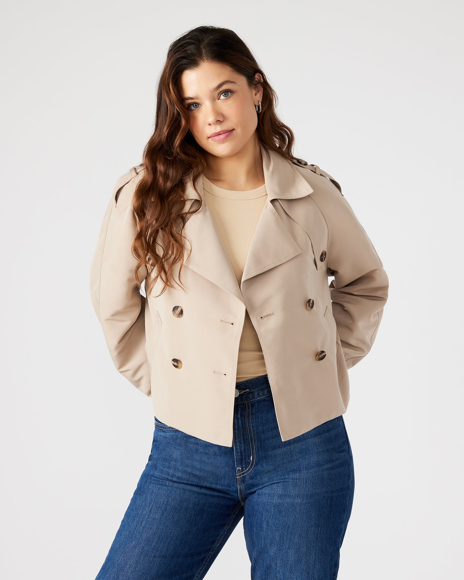 Close-up of double-breasted button closure and side pockets of cropped trench jacket.