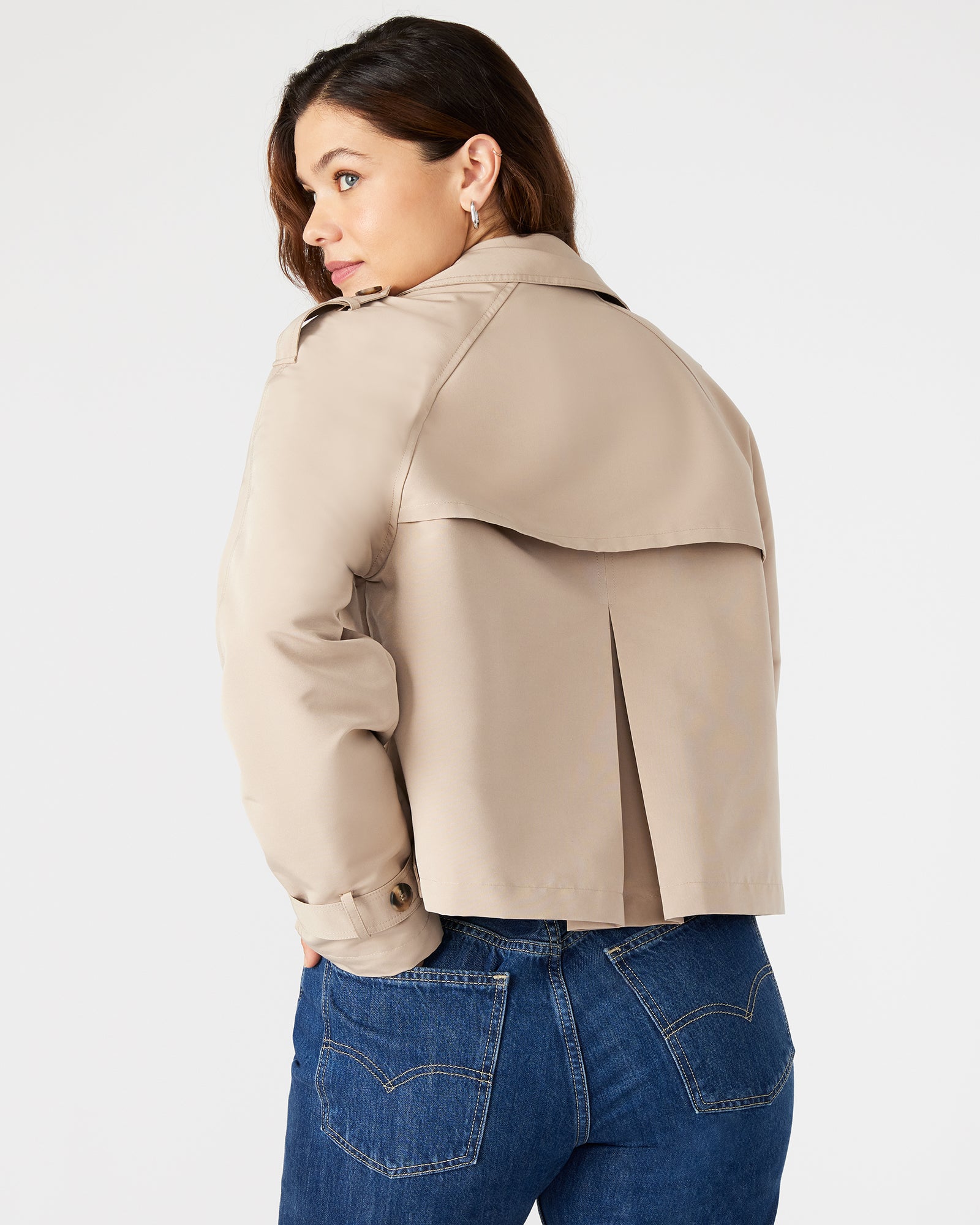 Front view of khaki cropped trench jacket on model in an urban setting.