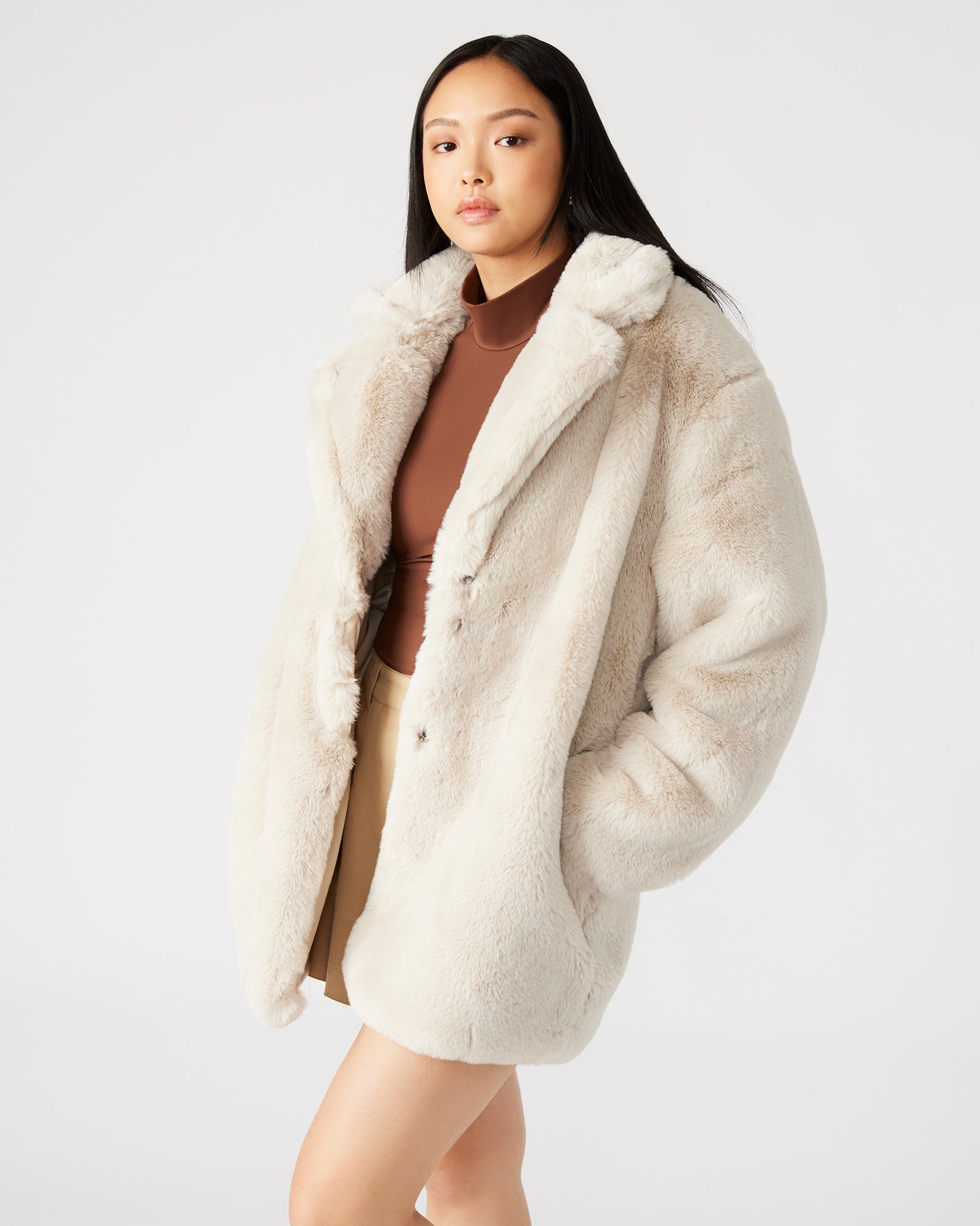 Model wearing a chic beige faux fur coat in a winter landscape.