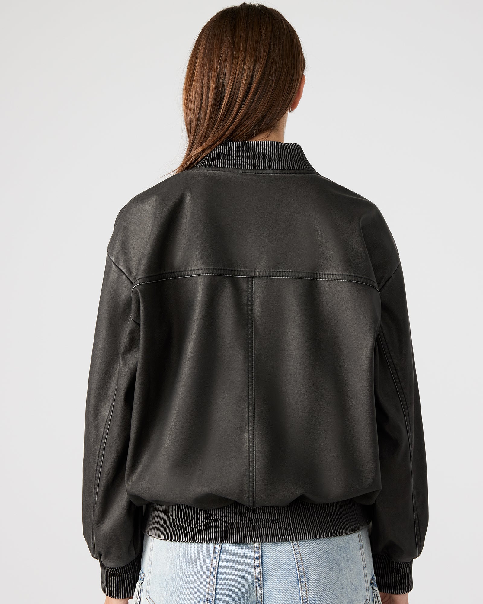 Front view of oversized faux leather jacket paired with denim on urban backdrop
