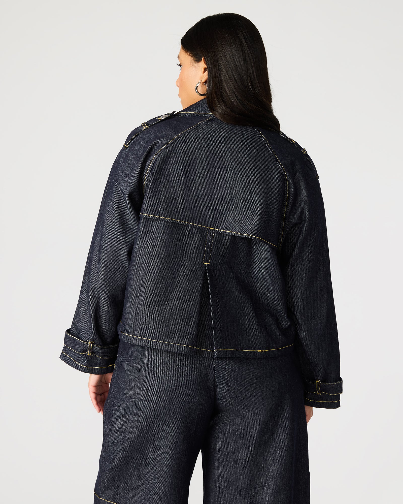Back view of cropped trench coat with pleated flap and shoulder epaulettes.