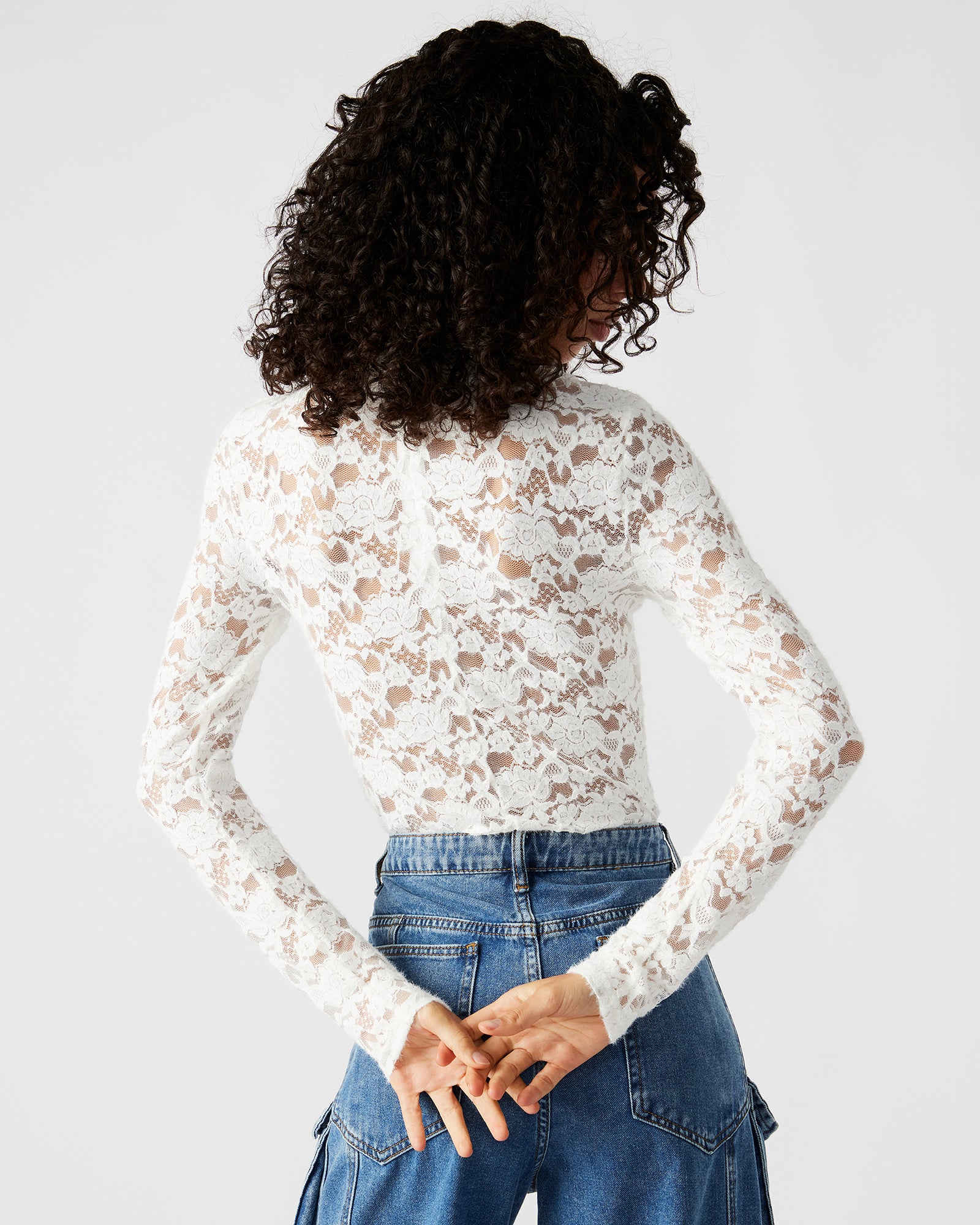 Front view of ivory sheer bodysuit with lace sleeves worn by model in a city setting.