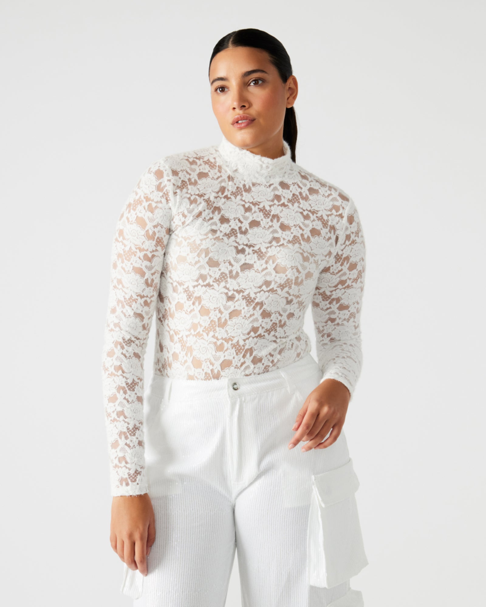 Front view of ivory sheer bodysuit with lace sleeves worn by model in a city setting.