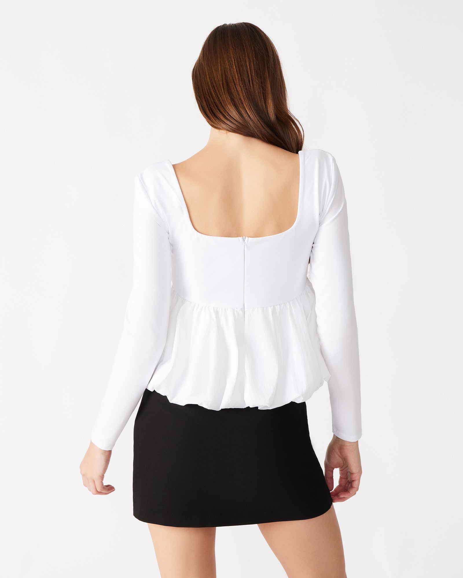 Model wearing a white peplum top with long sleeves for a sophisticated look
