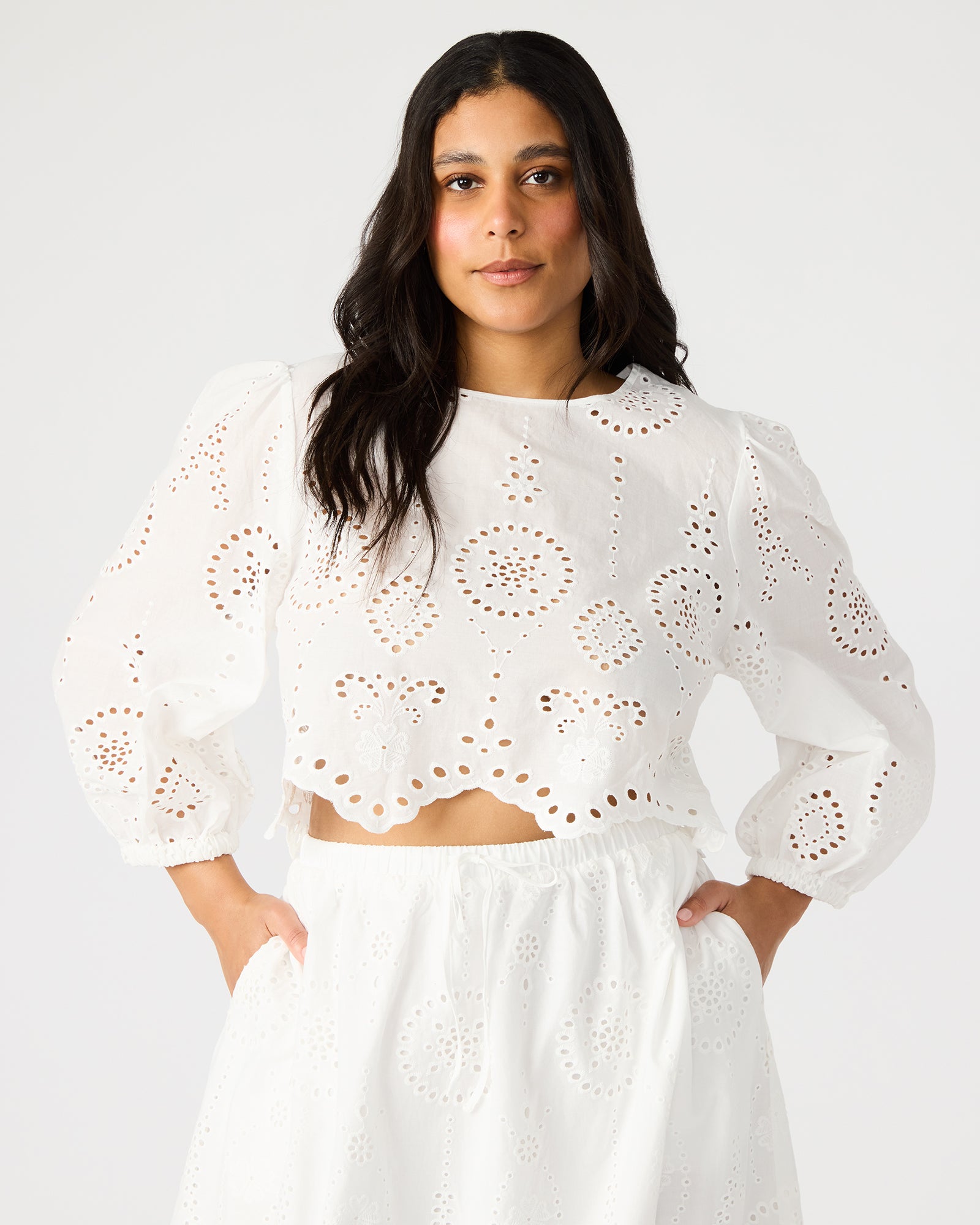 Front view of white crop top with eyelet details and long sleeves, styled casually