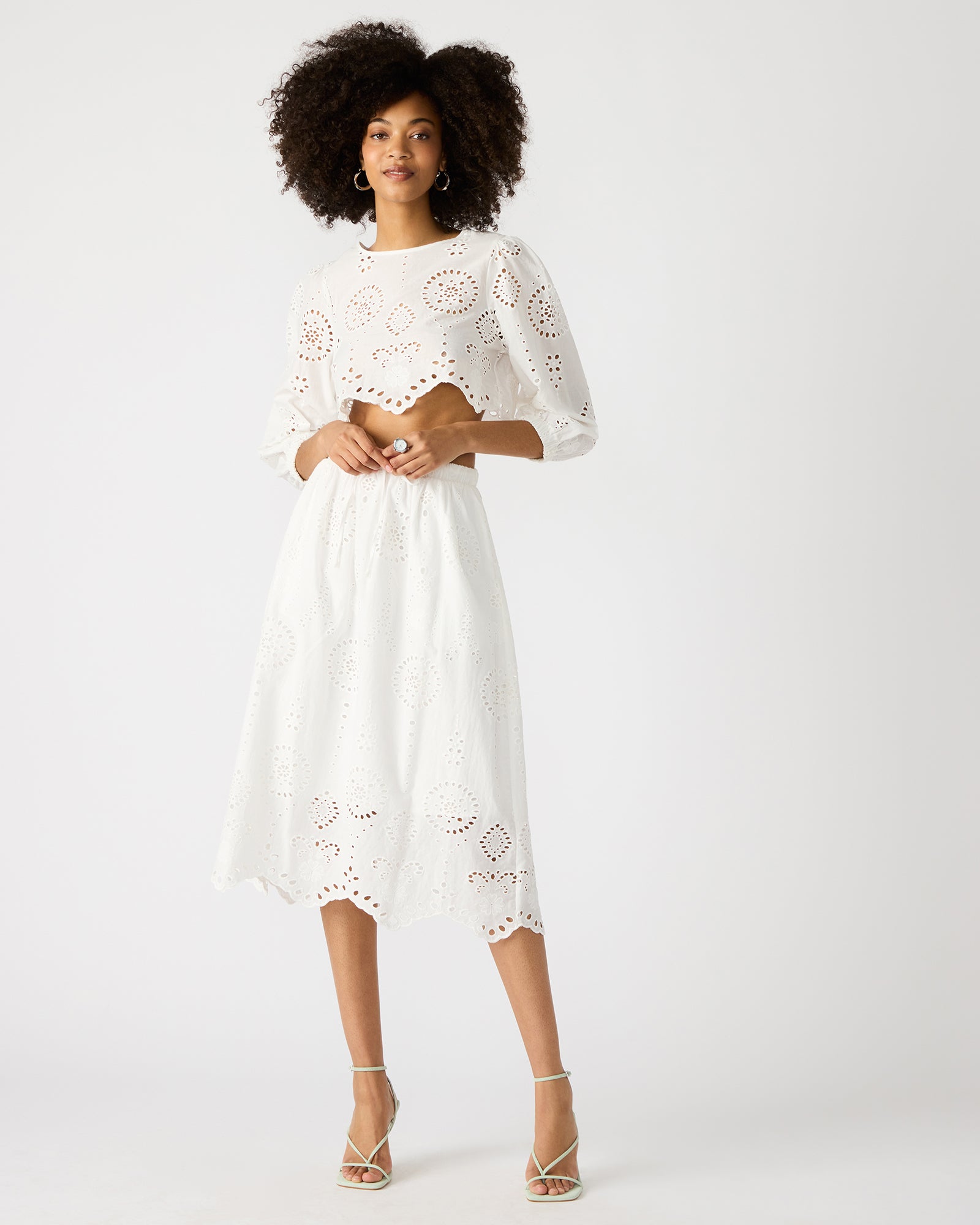 Front view of white linen midi skirt with eyelet detailing, styled with a straw bag