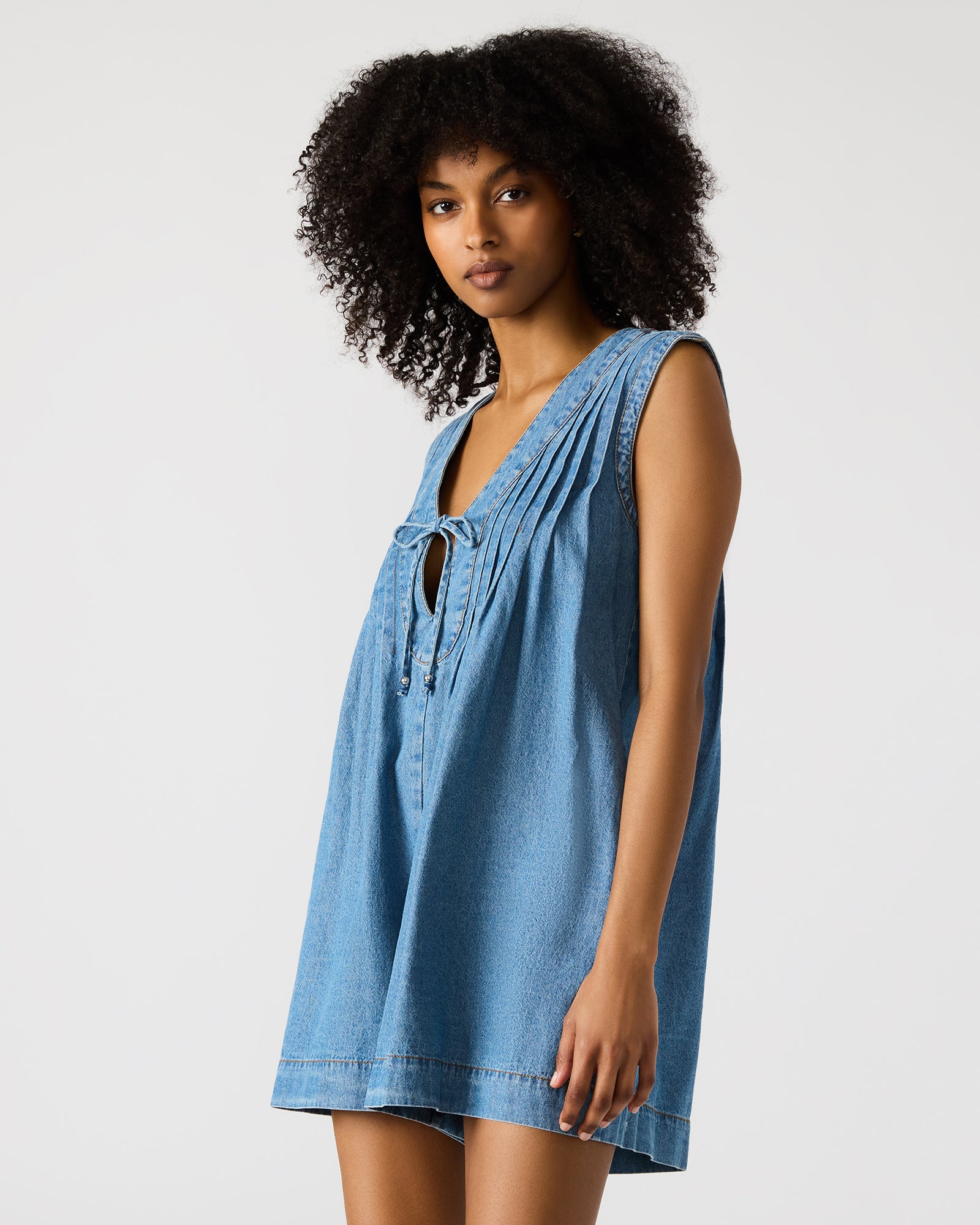 Side angle of the white denim romper tied at the waist for a fitted look.