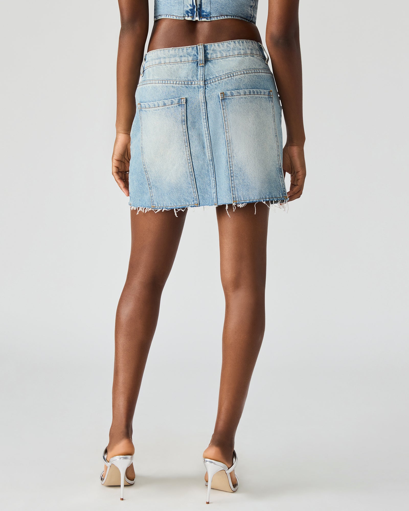 Model wearing ERAS denim mini skirt with rhinestones, standing outdoors