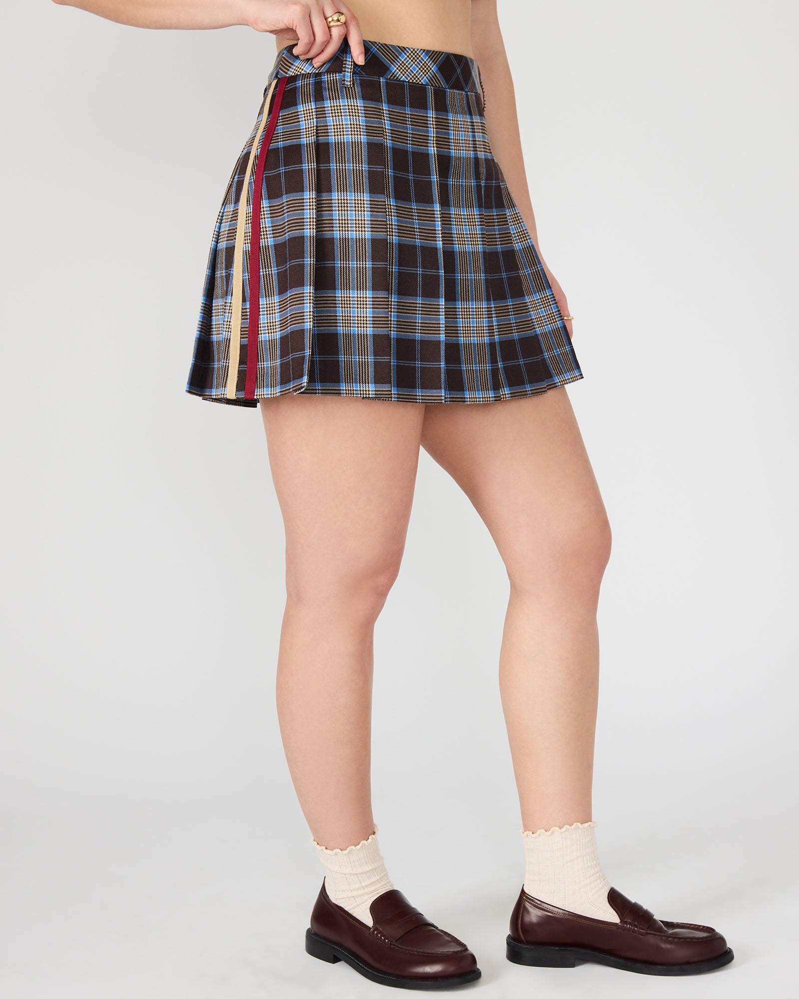 Model wearing the brown plaid pleated mini skirt paired with a simple top for a daytime look