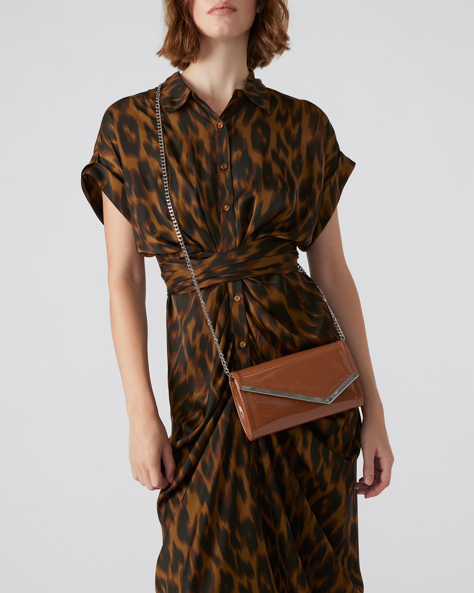 Close-up of tan patent leather clutch bag showing asymmetrical flap detail