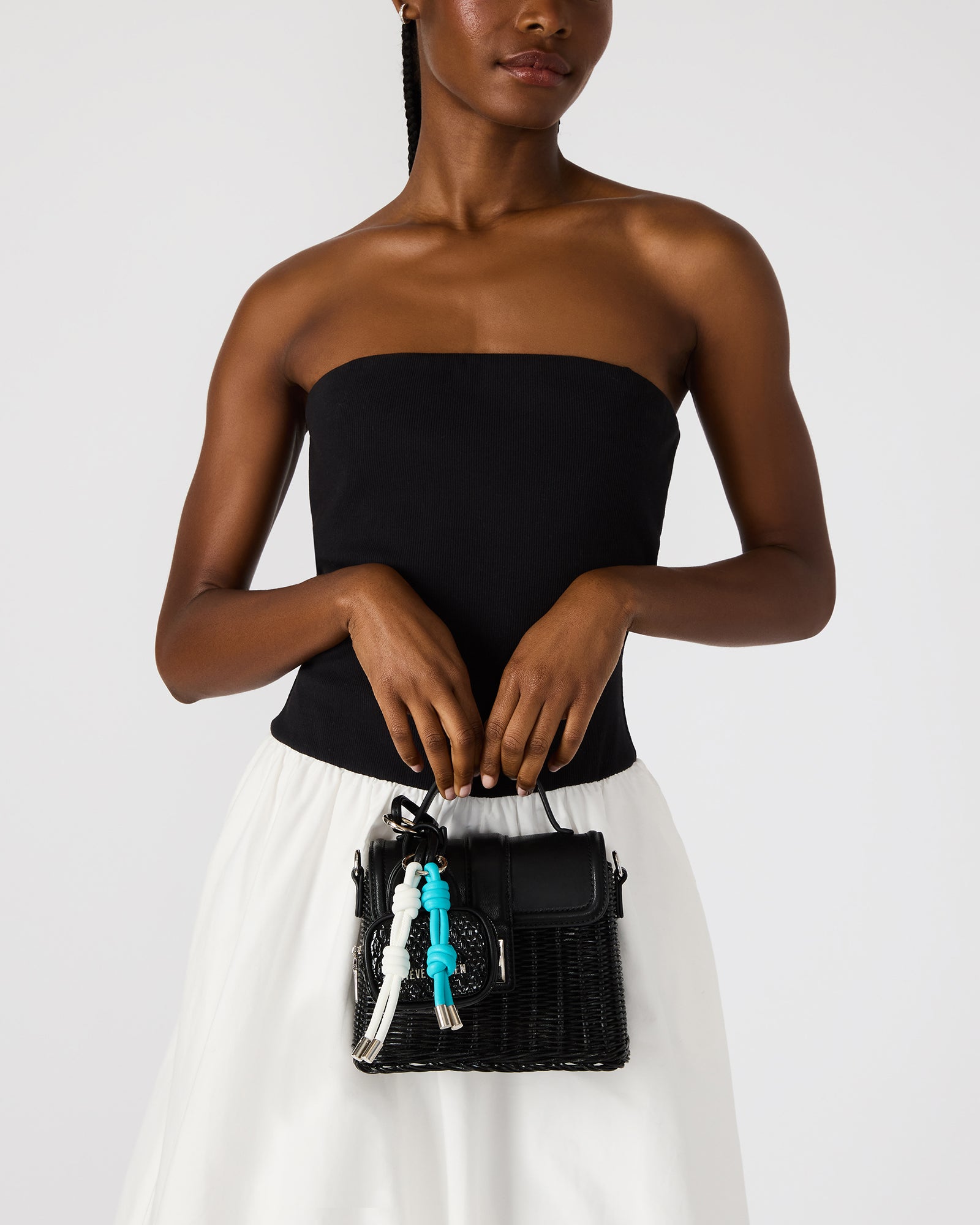Black bag charm attached to leather tote, shown from side angle in NYC setting