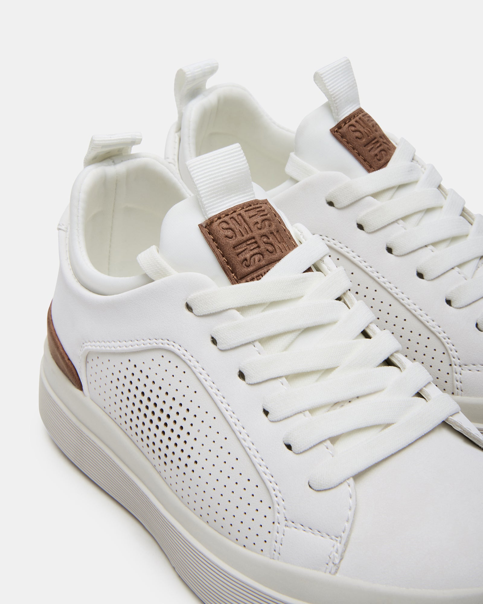 Side profile of mens white leather sneakers styled with dark jeans outdoors