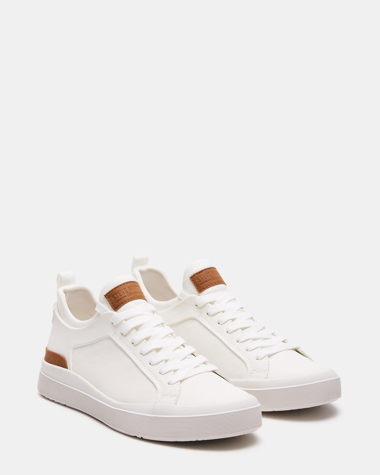 Side profile of mens white leather sneakers styled with dark jeans outdoors