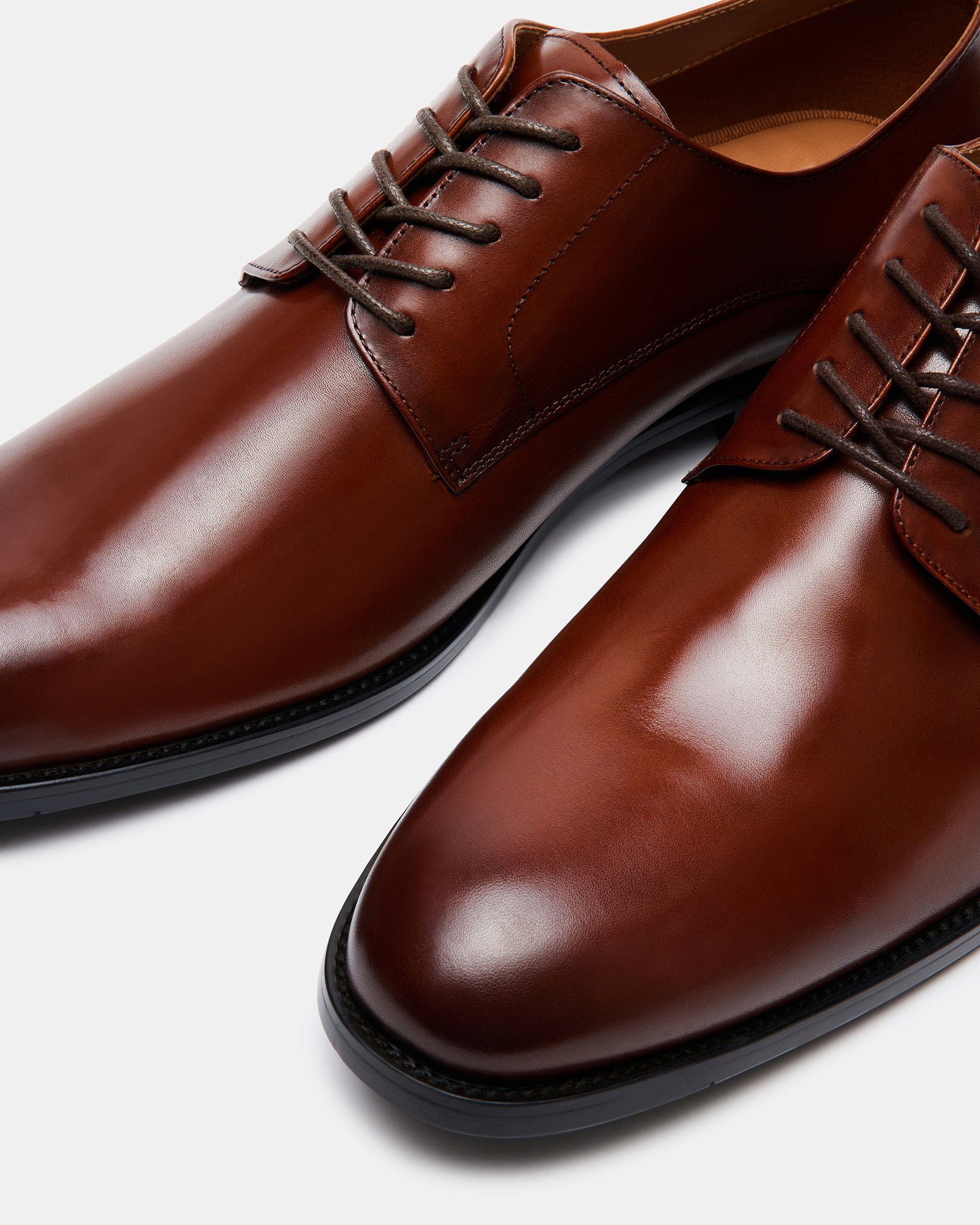 Side view of polished tan leather derby shoes on a wooden floor