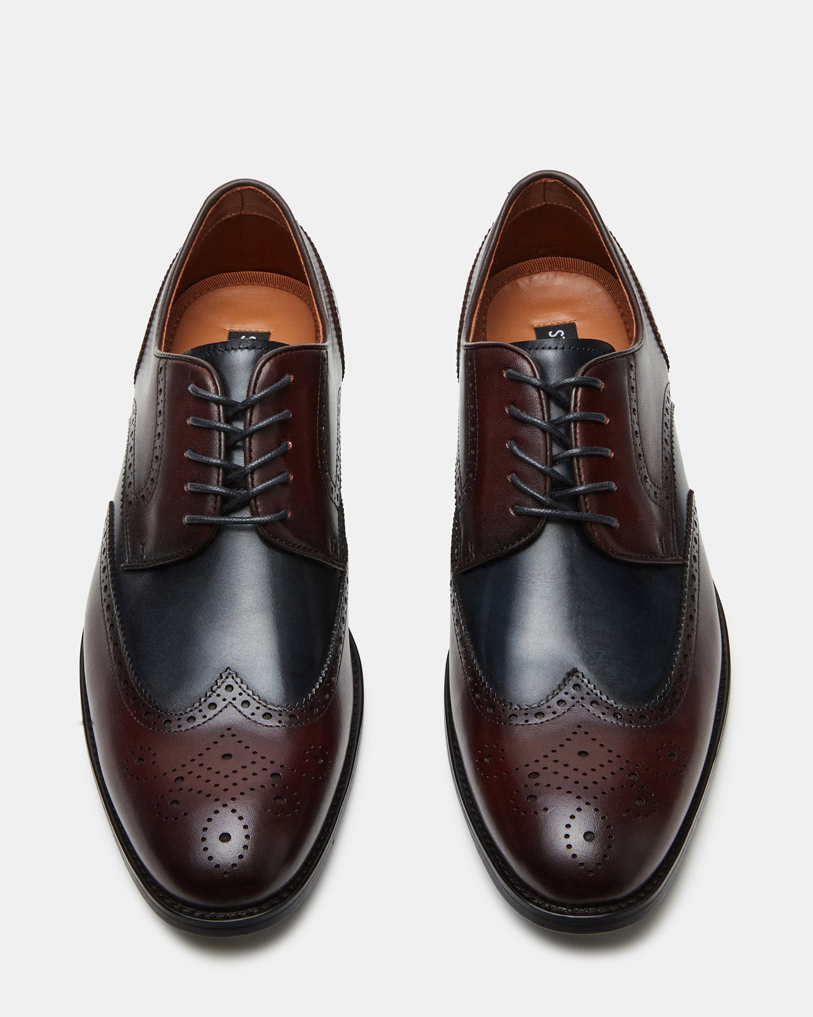 Top view of mens wingtip shoes styled with formal attire on dark wood floor.