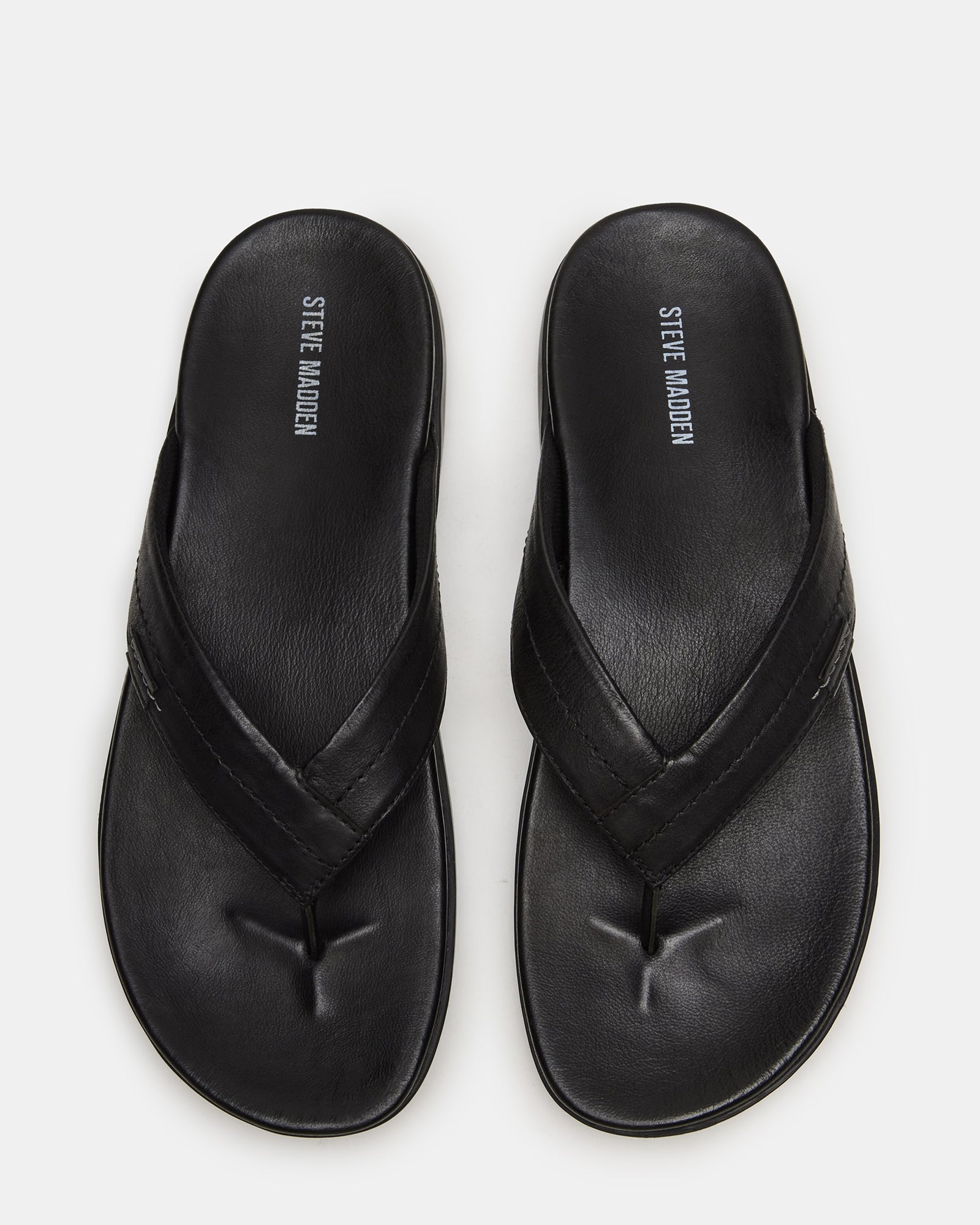 Side view of Emmett black leather thong sandals on a sunny patio.