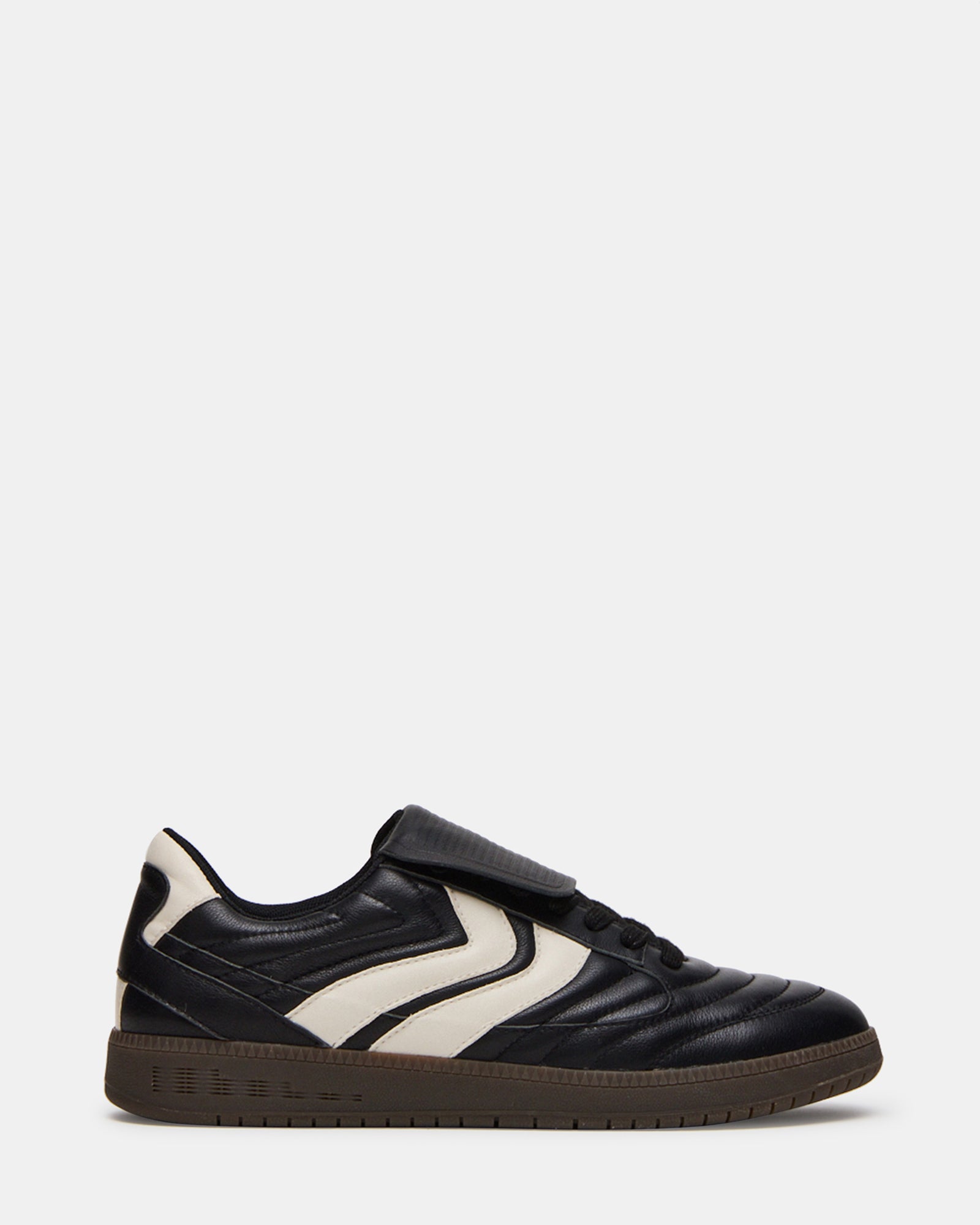 Side view of men's black sneakers with textured sole on city pavement