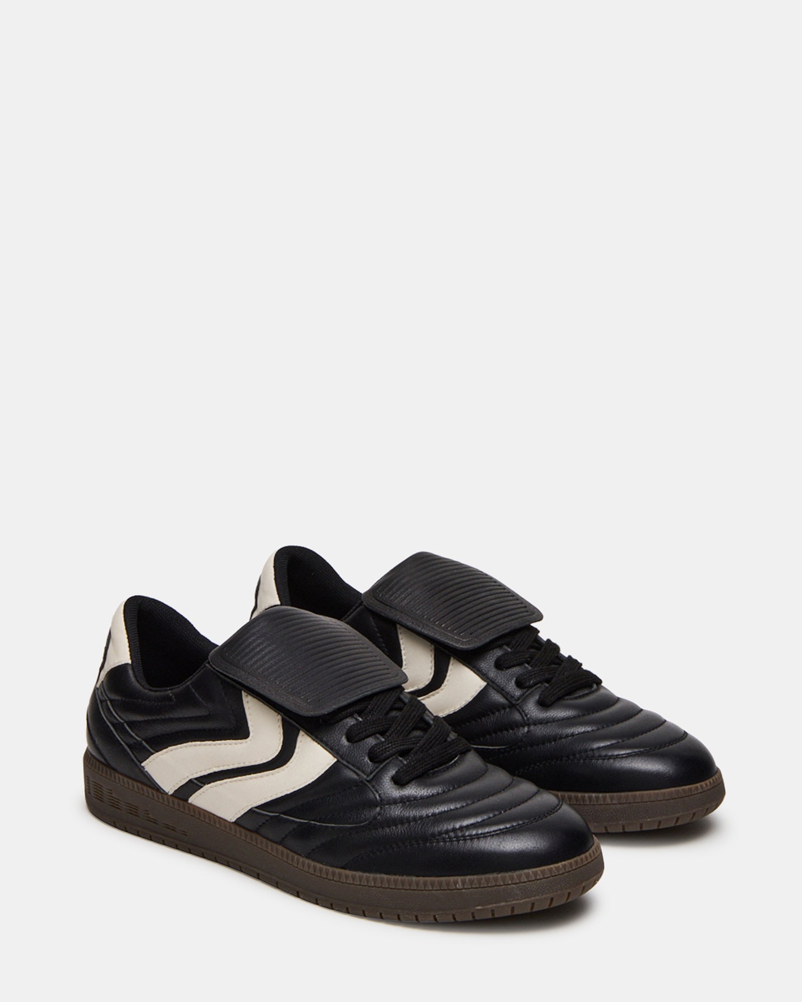 Mens black leather sneakers worn casually with rolled jeans in an urban setting