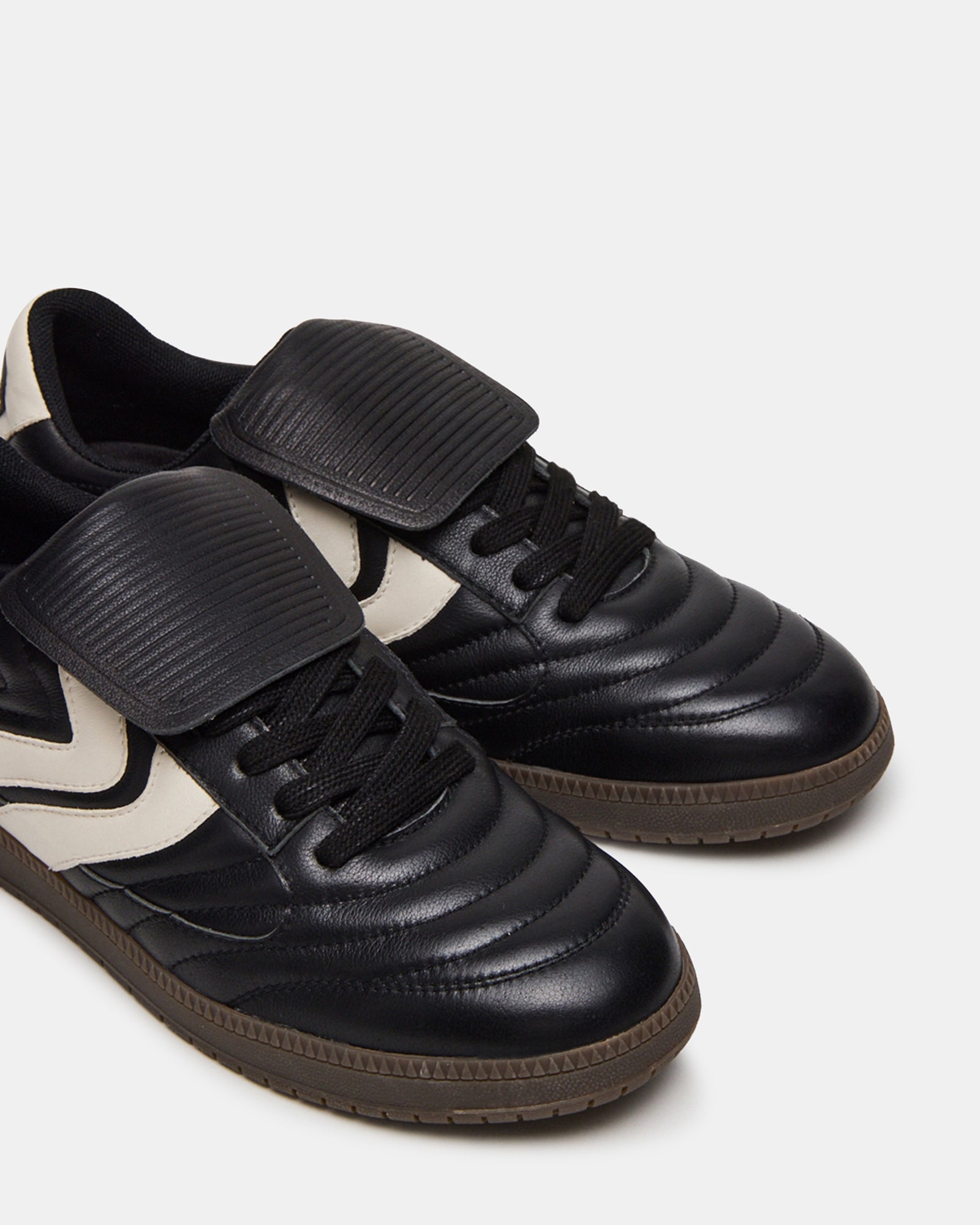 Side view of mens black sneakers with textured sole on city pavement