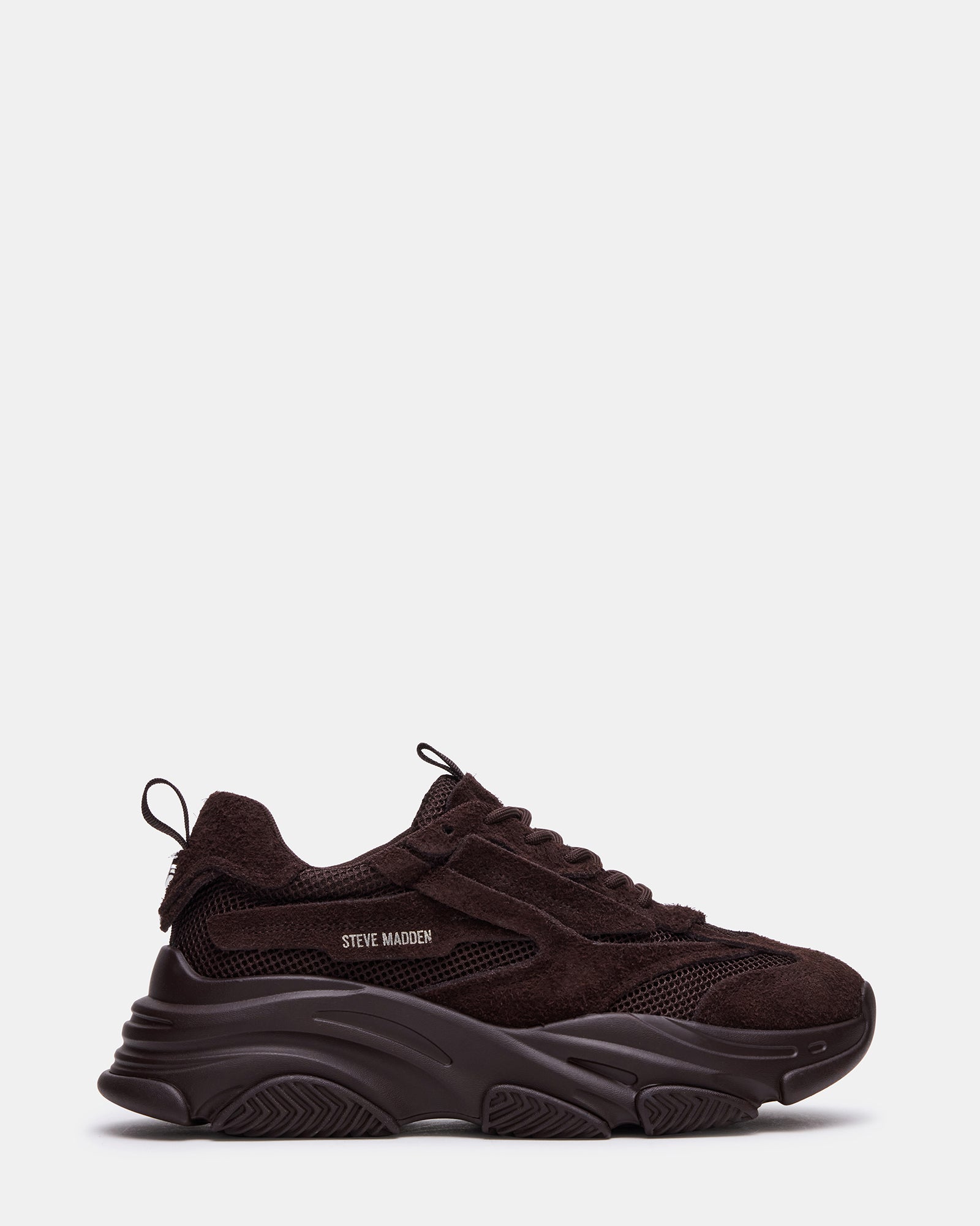 Side view of brown suede sneakers on a city sidewalk.