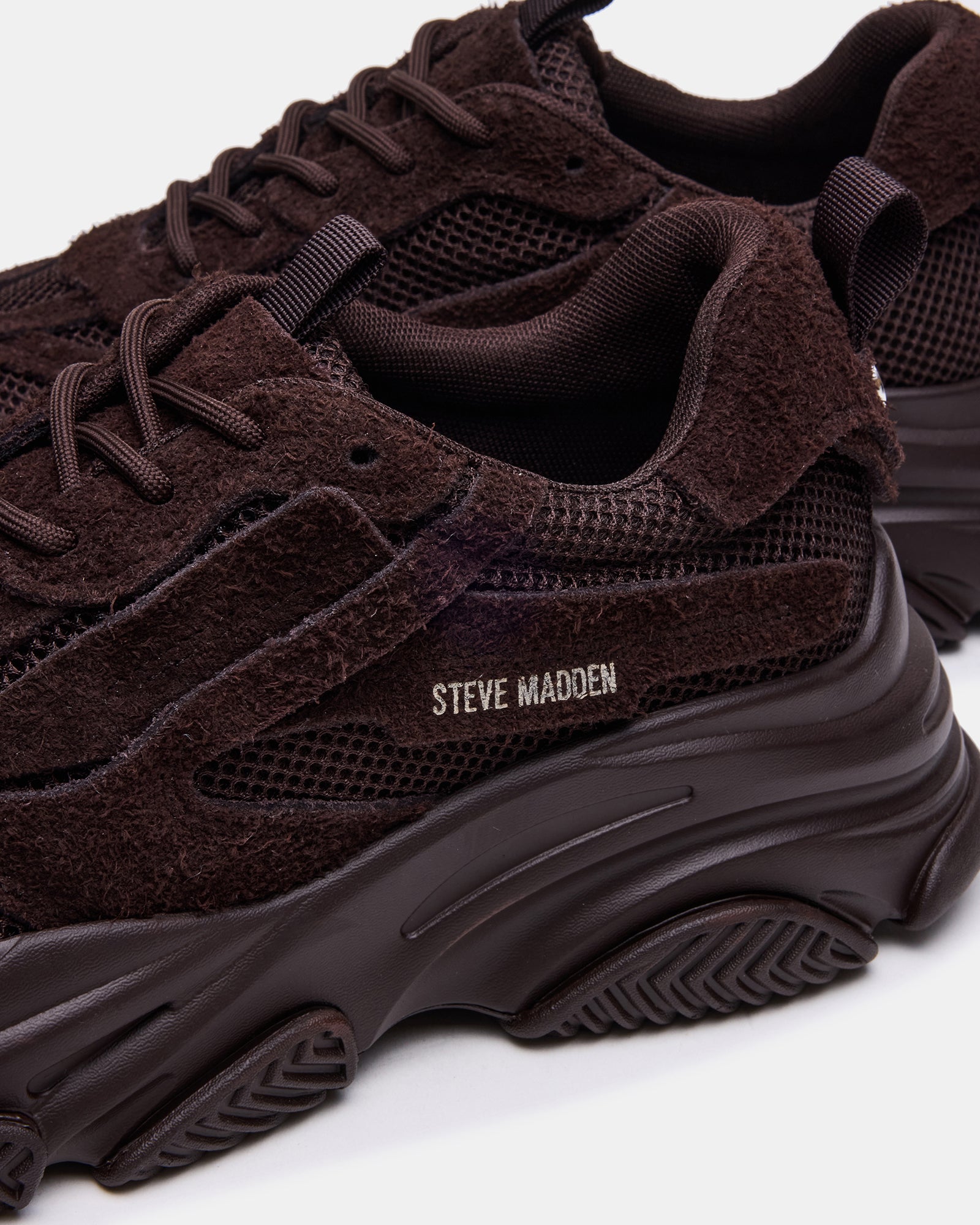 Side view of brown suede sneakers on a city sidewalk.