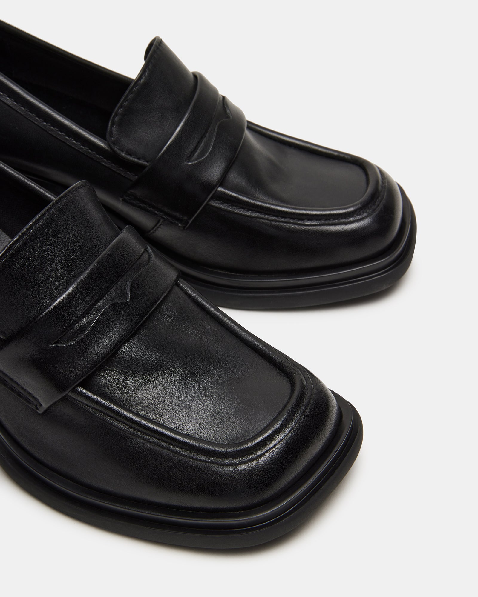 Side view of Baxter black leather loafers with block heel on a stylish backdrop.