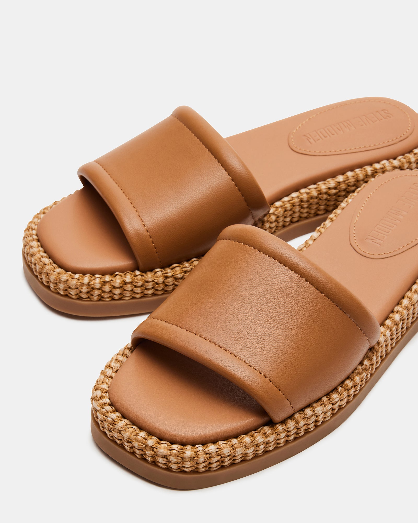 Close-up of tan leather slide sandals showing raffia platform and square toe