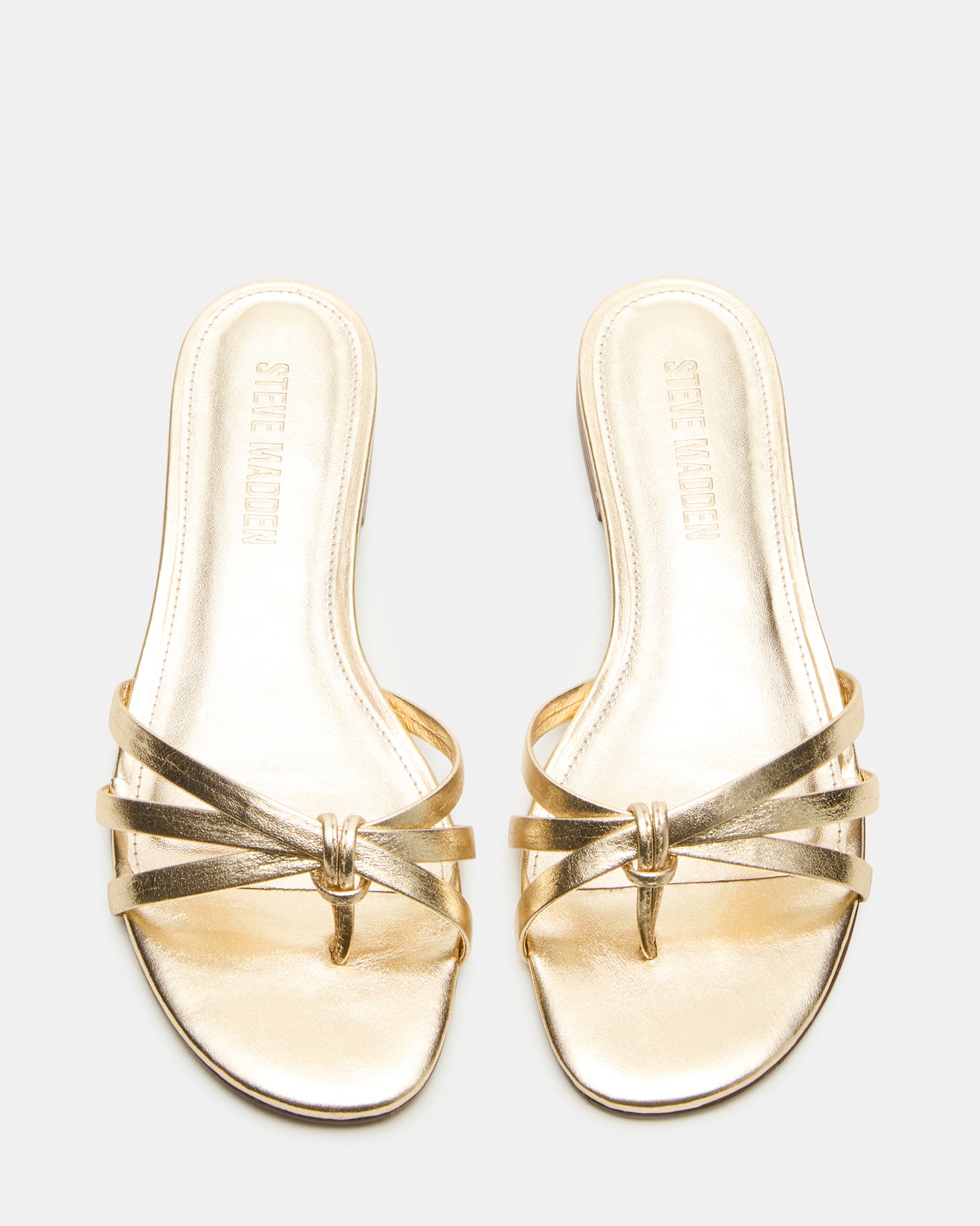 Model wearing gold strappy flat sandals at a summer outdoor event.