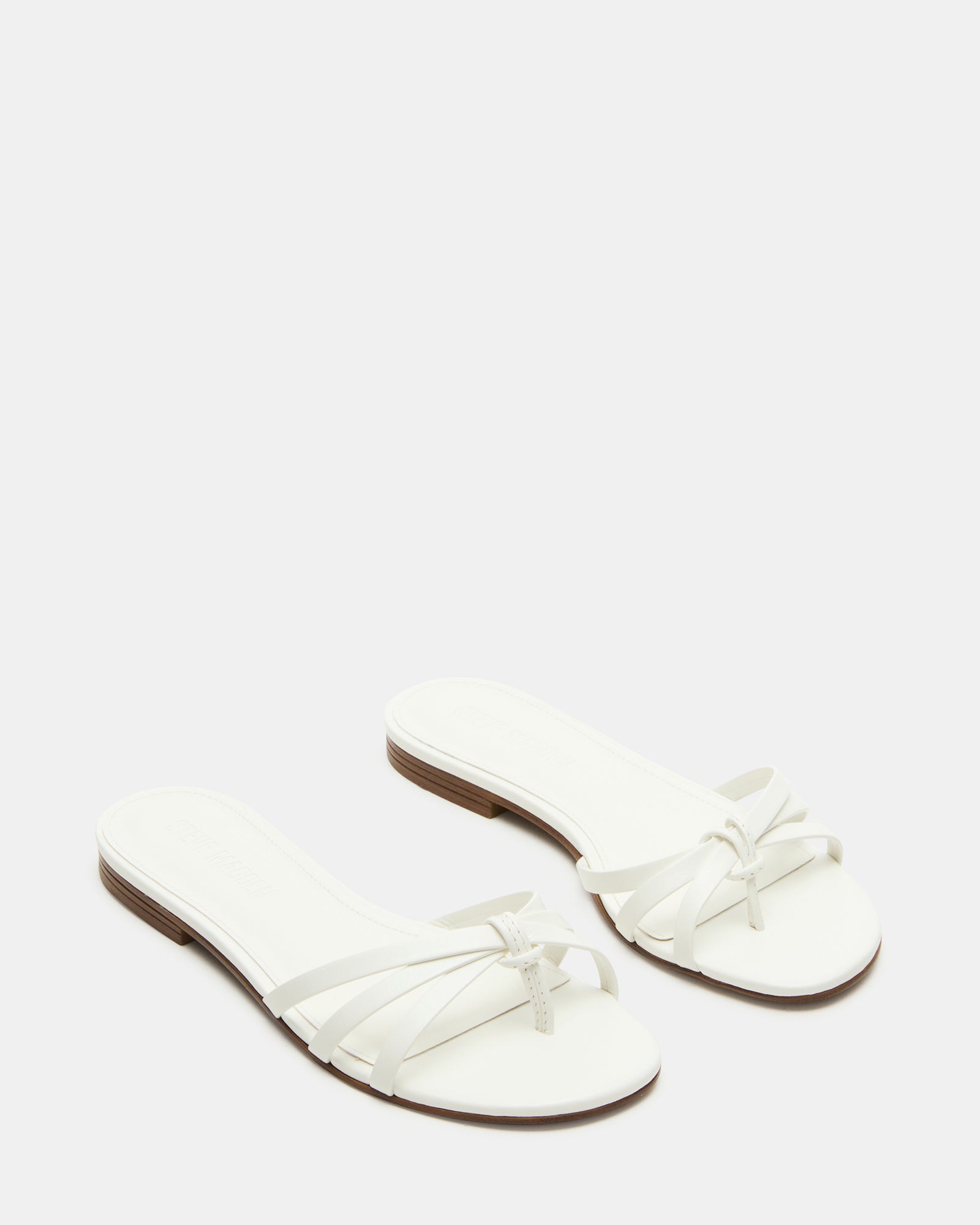 Stylish white sandals worn with a summer dress in a garden setting.