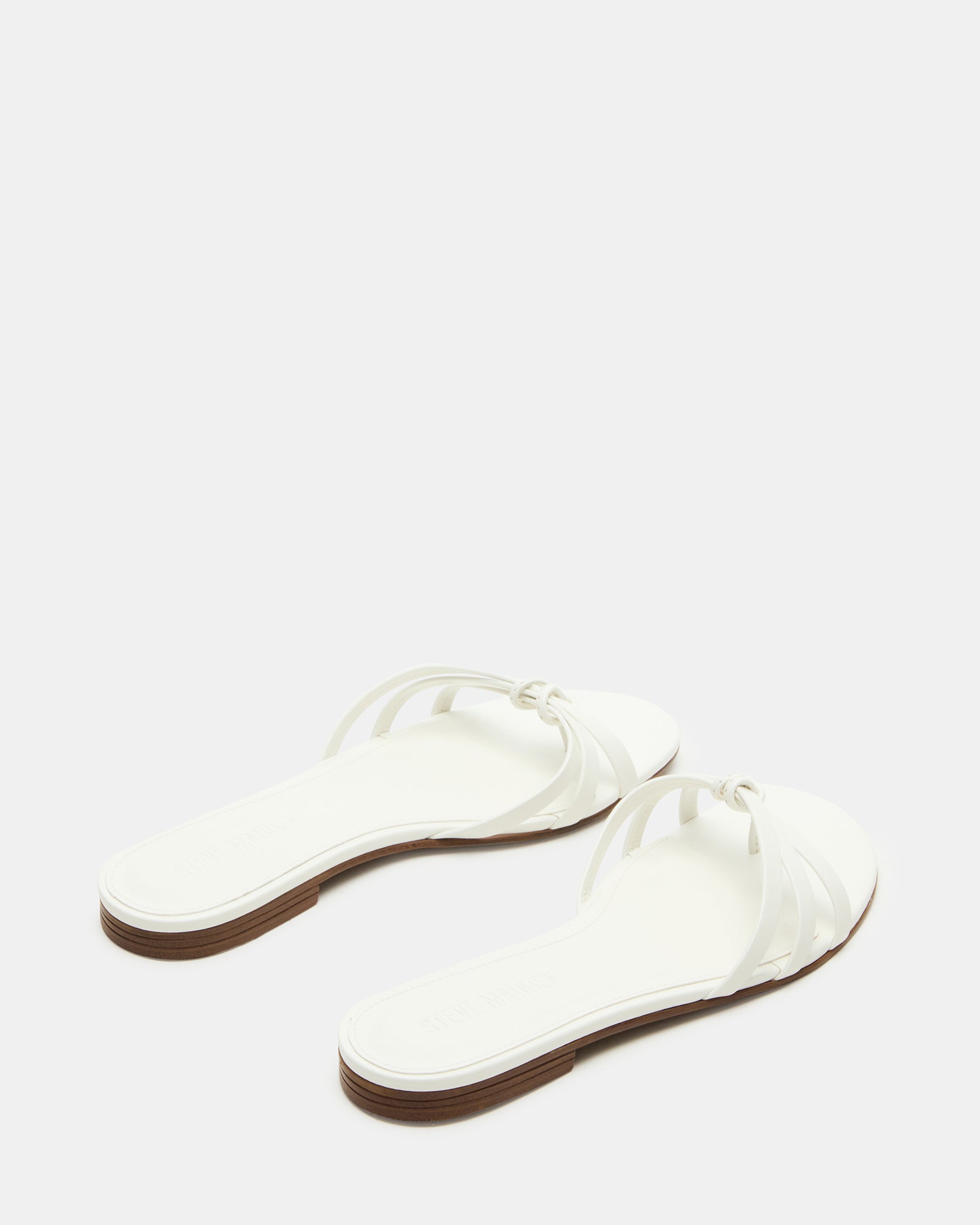 Stylish white sandals worn with a summer dress in a garden setting.