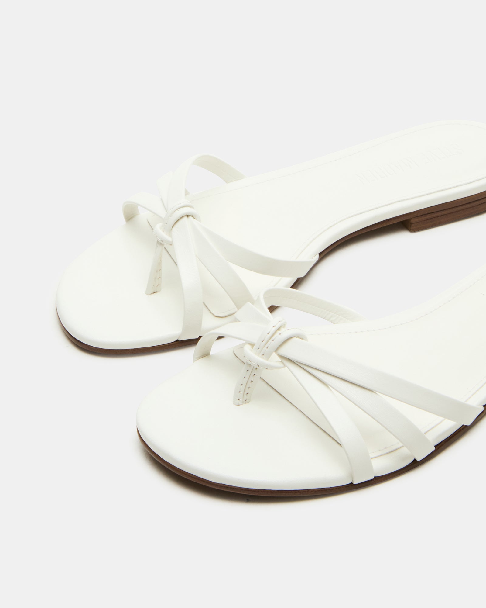 Calissi white wedge sandals displayed on a model at a beach party.