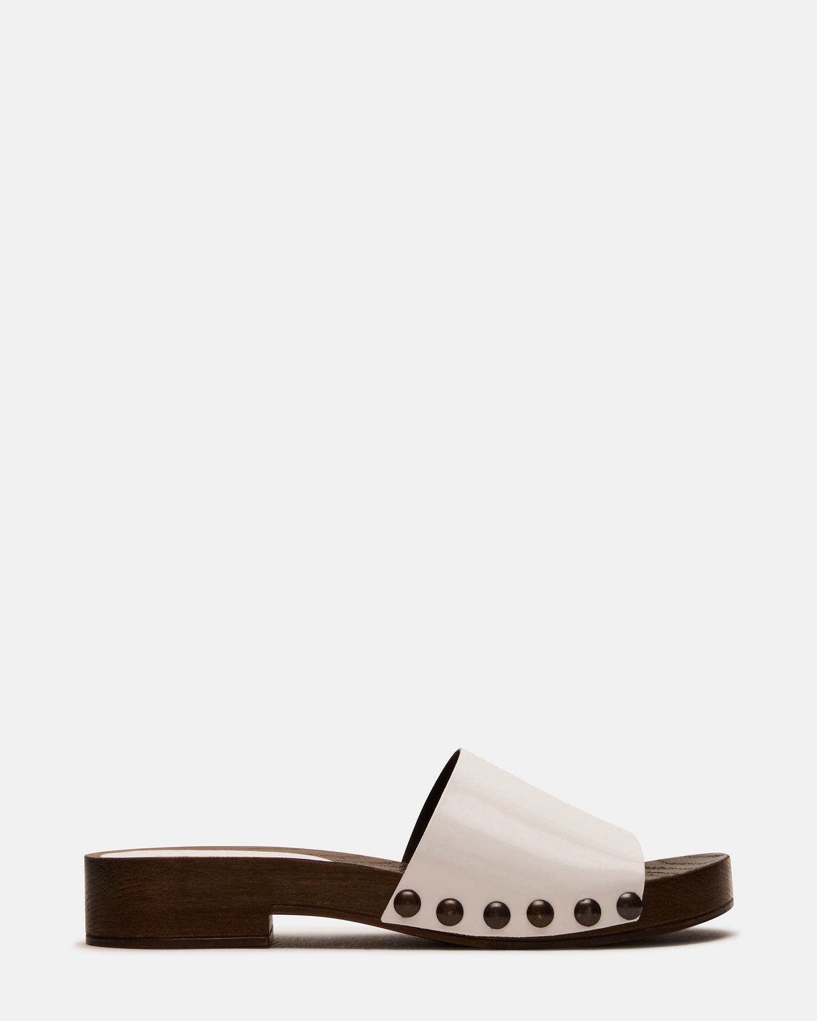 Front view of white patent leather studded slide sandals on a wooden deck