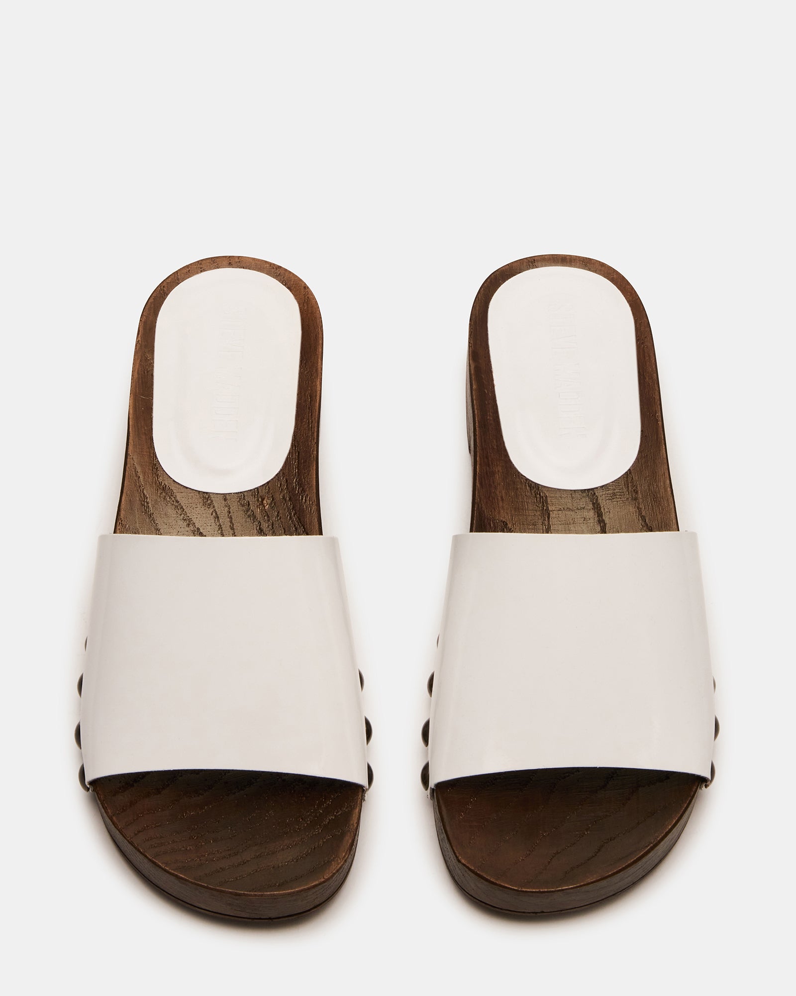 Front view of white patent leather studded slide sandals on a wooden deck