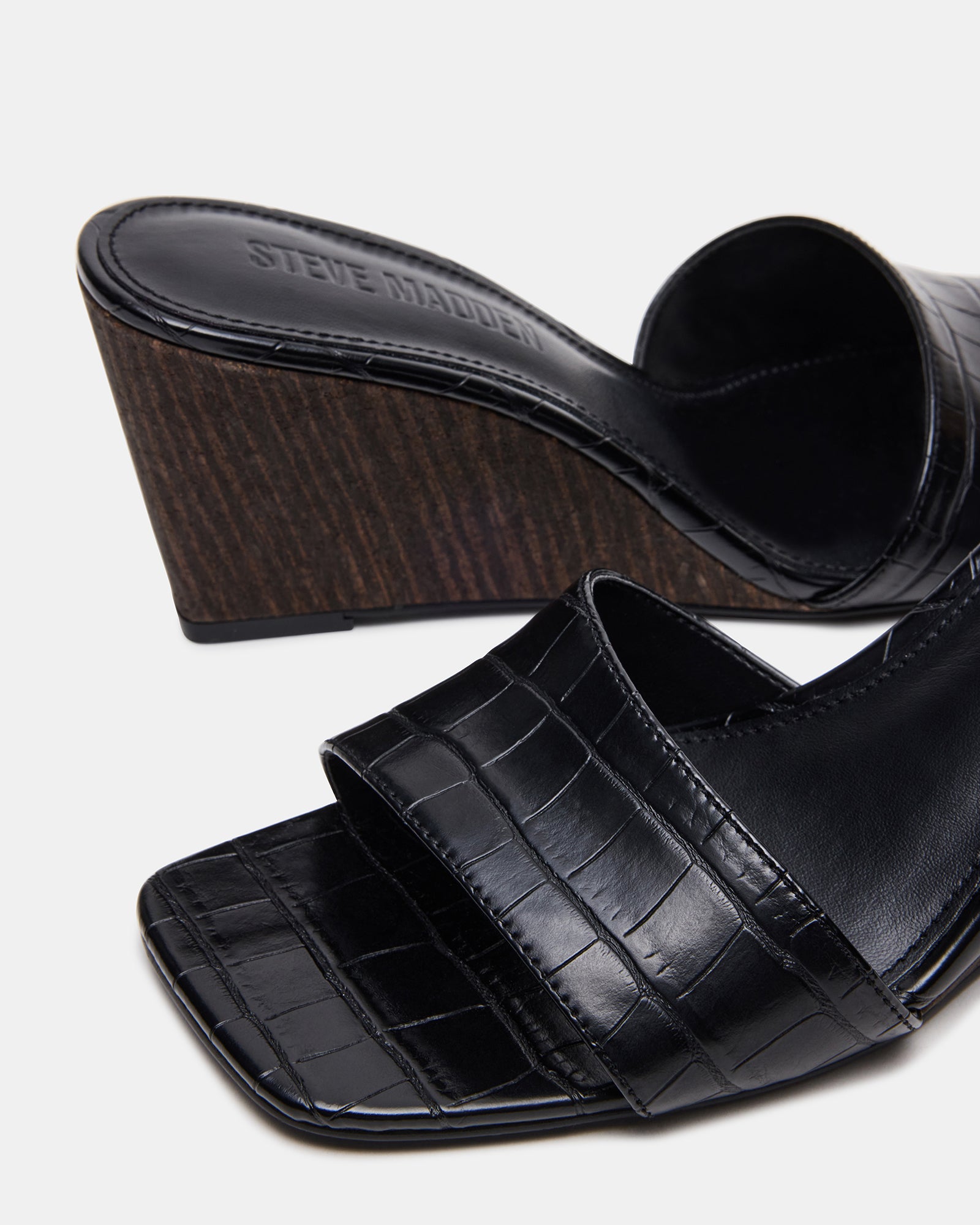 Close-up of crocodile-embossed detailing on brown sandals wedge heel.