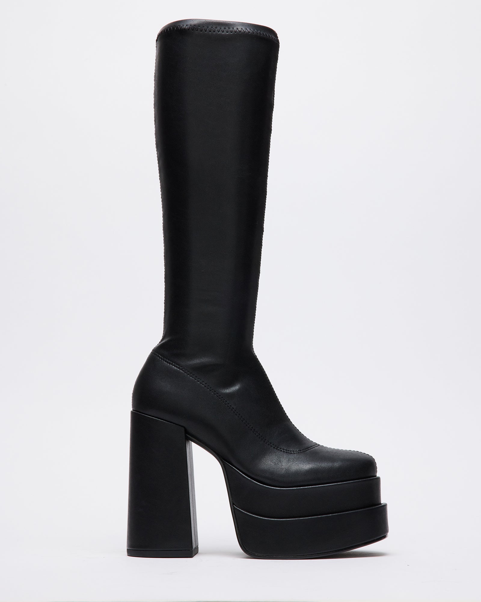 Black vegan leather knee boots on a wooden floor, showcasing the block heel.