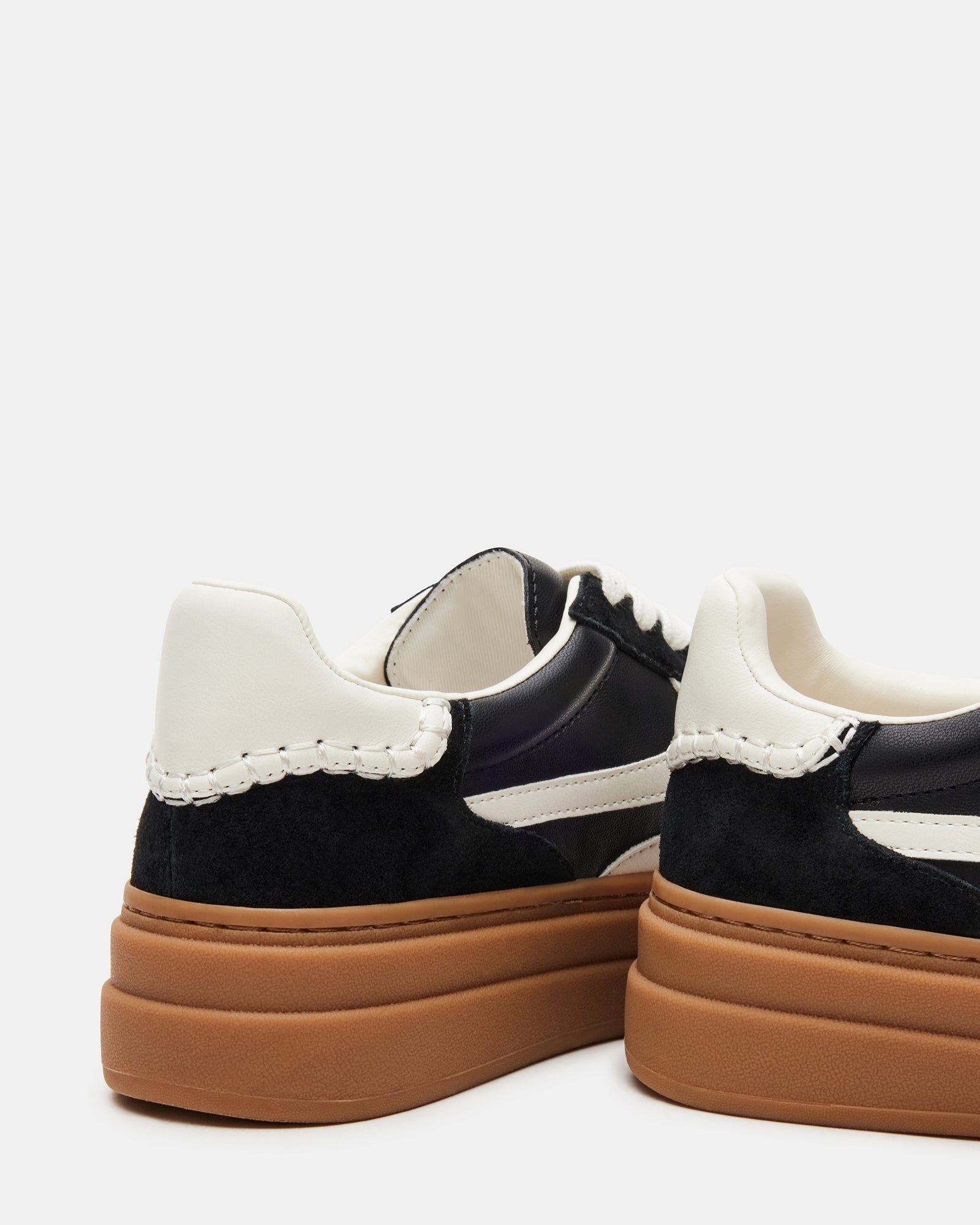 Side view of DODGE black and white sneakers on a city sidewalk.