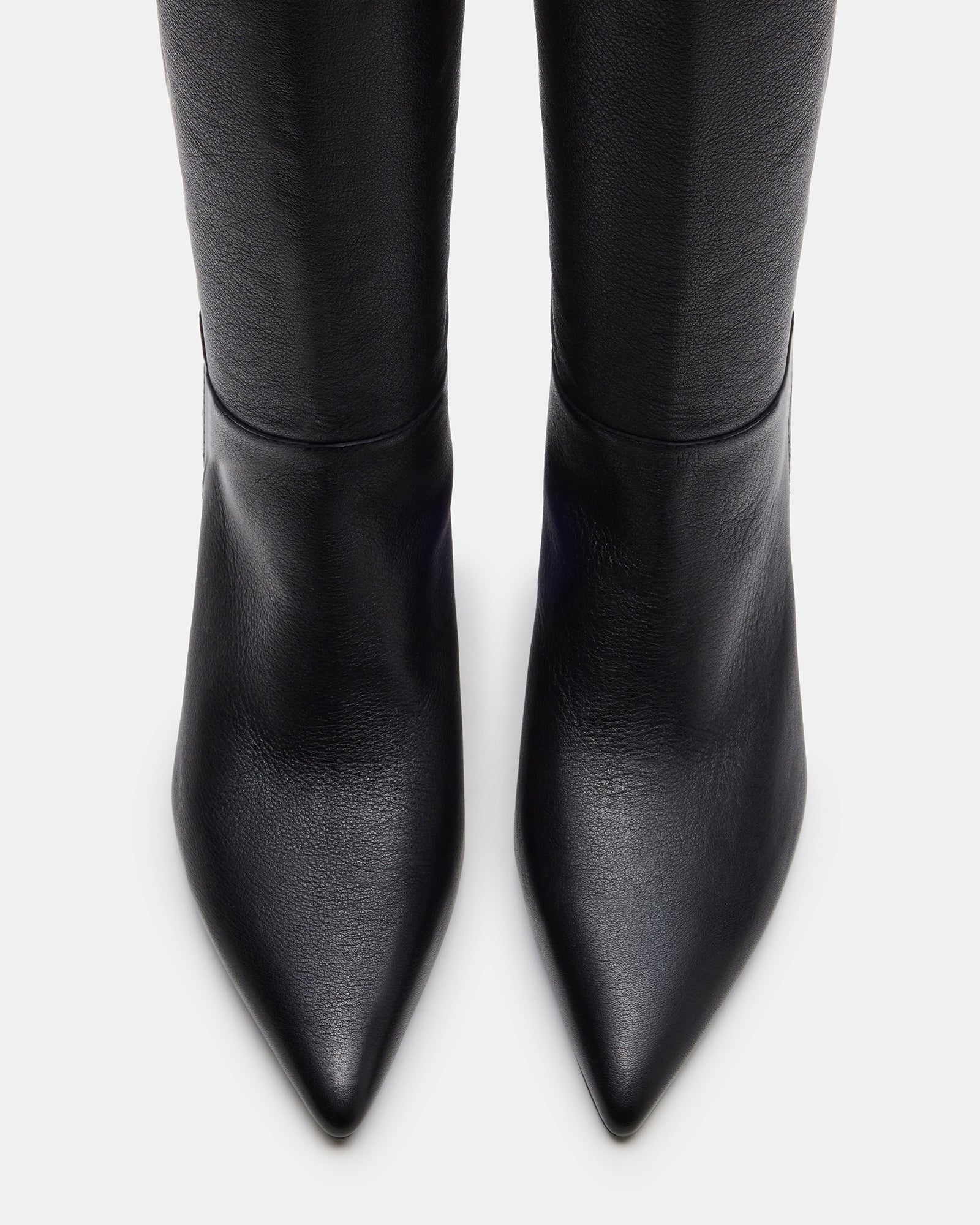 Side angle of black pointed toe boots styled over skinny jeans in urban fall setting.