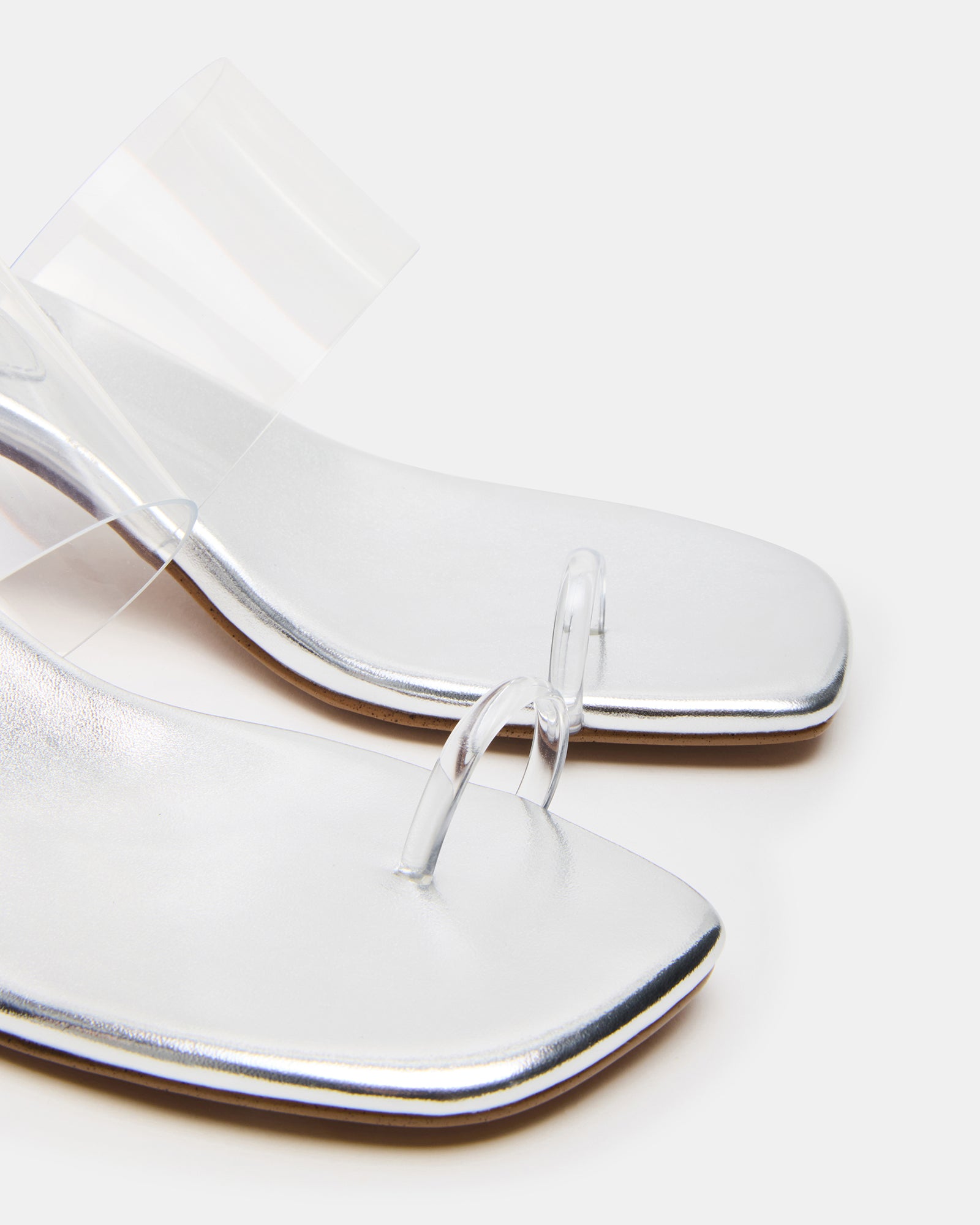 Model wearing white mule high heels in a fashionable outdoor setting.