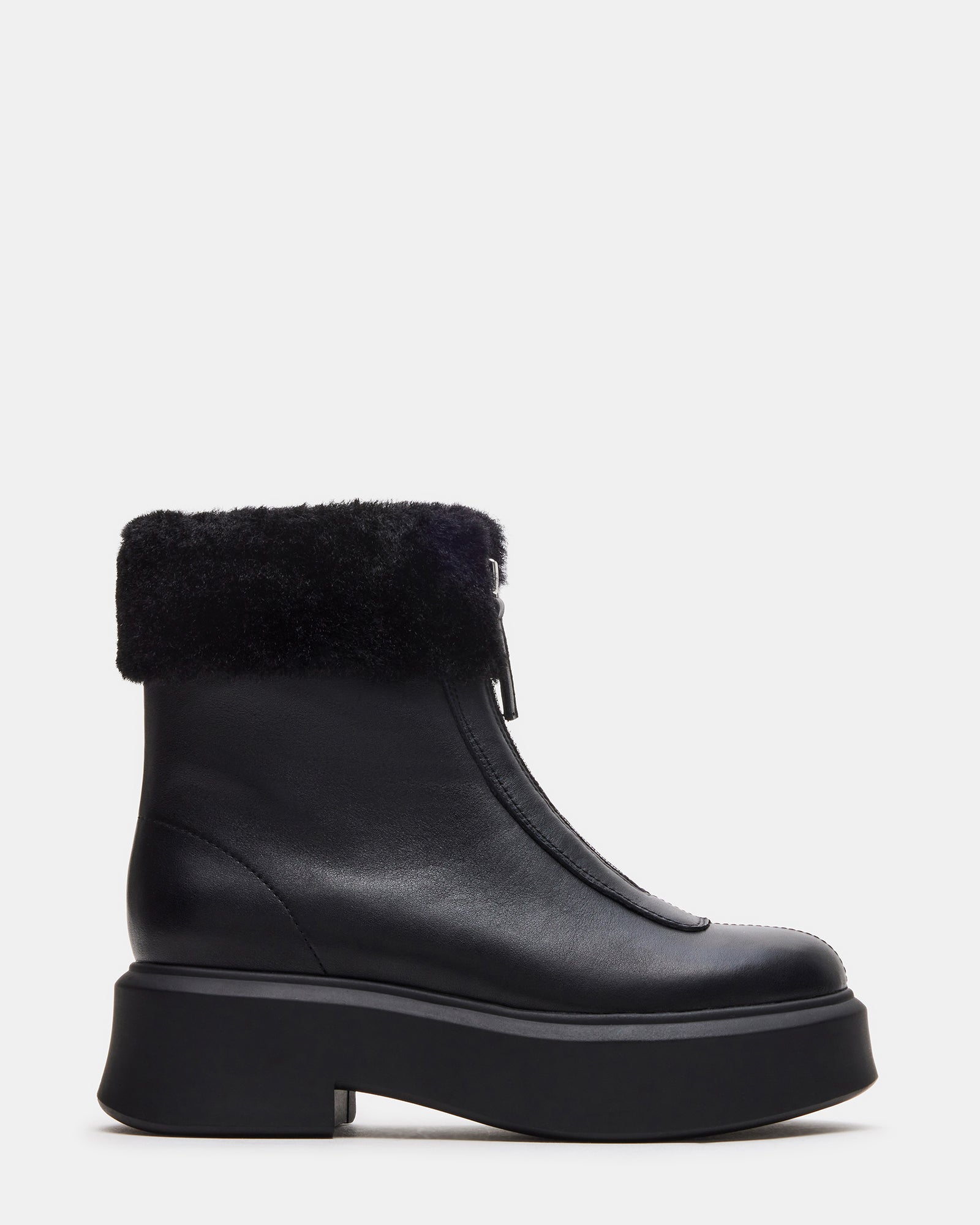 Side profile of black leather boots with faux fur trim on snowy pavement