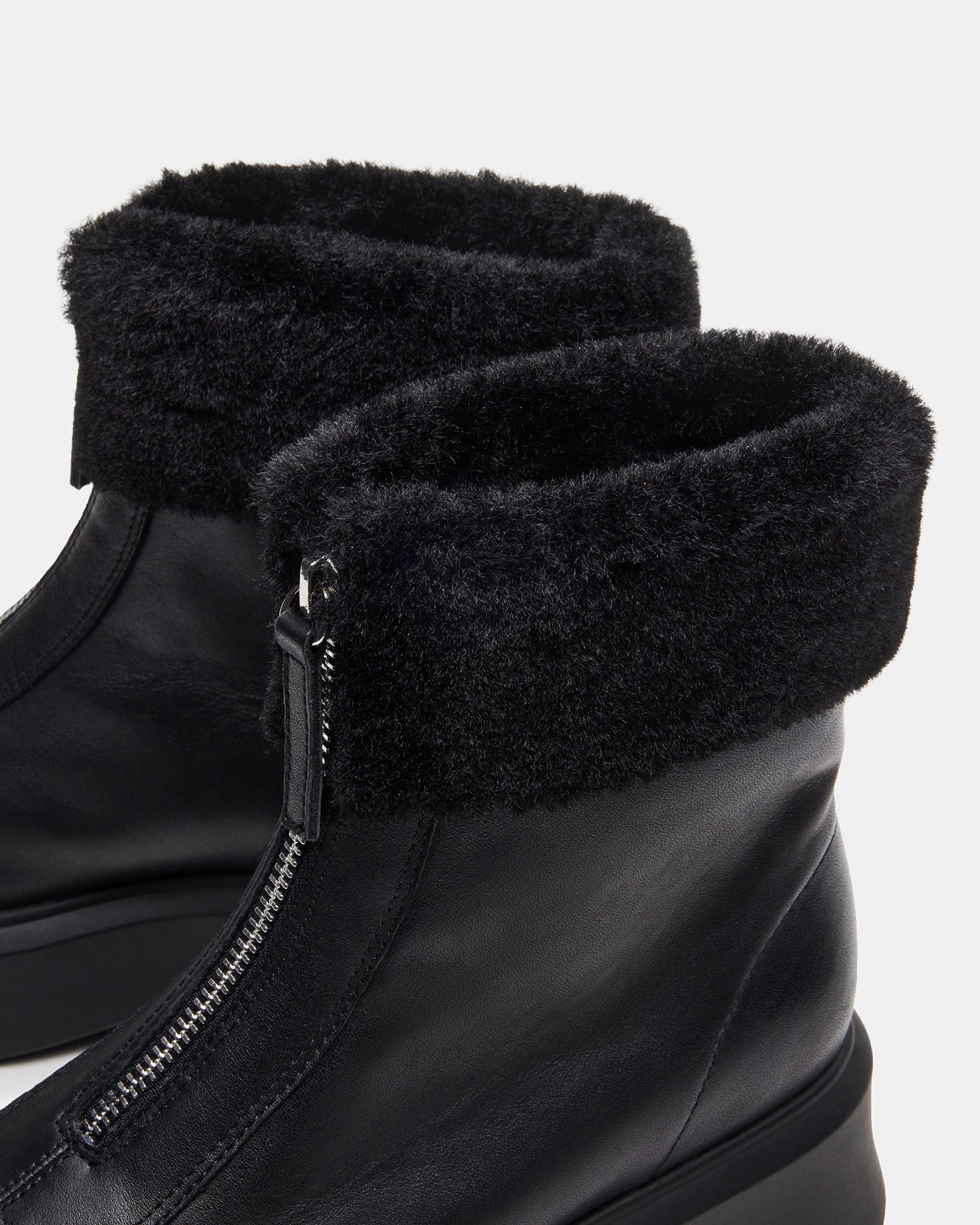Side profile of black leather boots with faux fur trim on snowy pavement