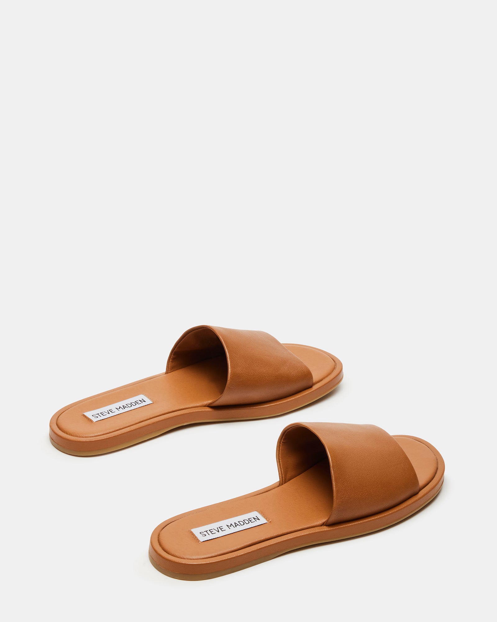 Model wearing brown leather slide sandals in a summer setting.