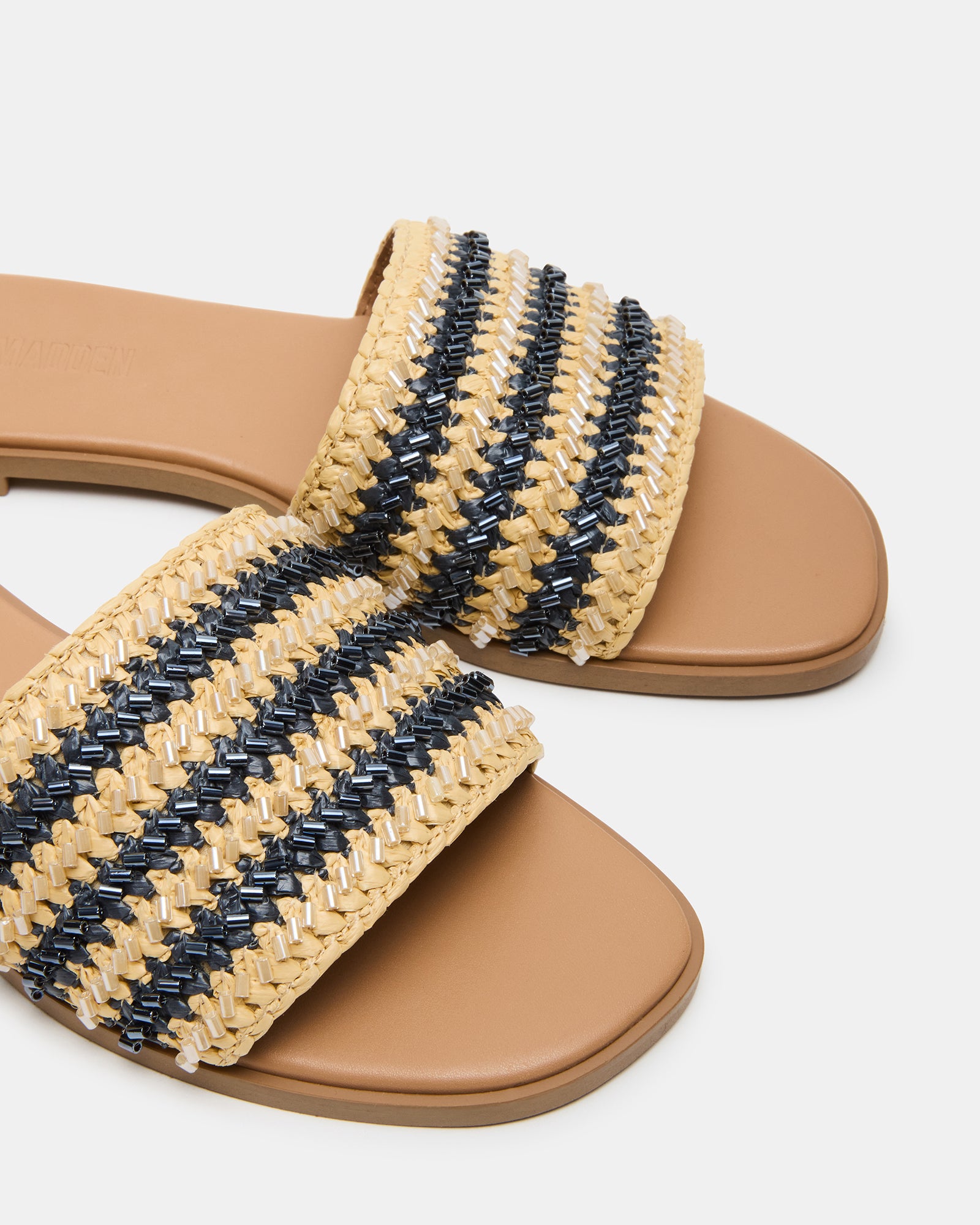 Close-up of the raffia upper on Kooper flat slide sandals in navy multi, resting on a linen cushion