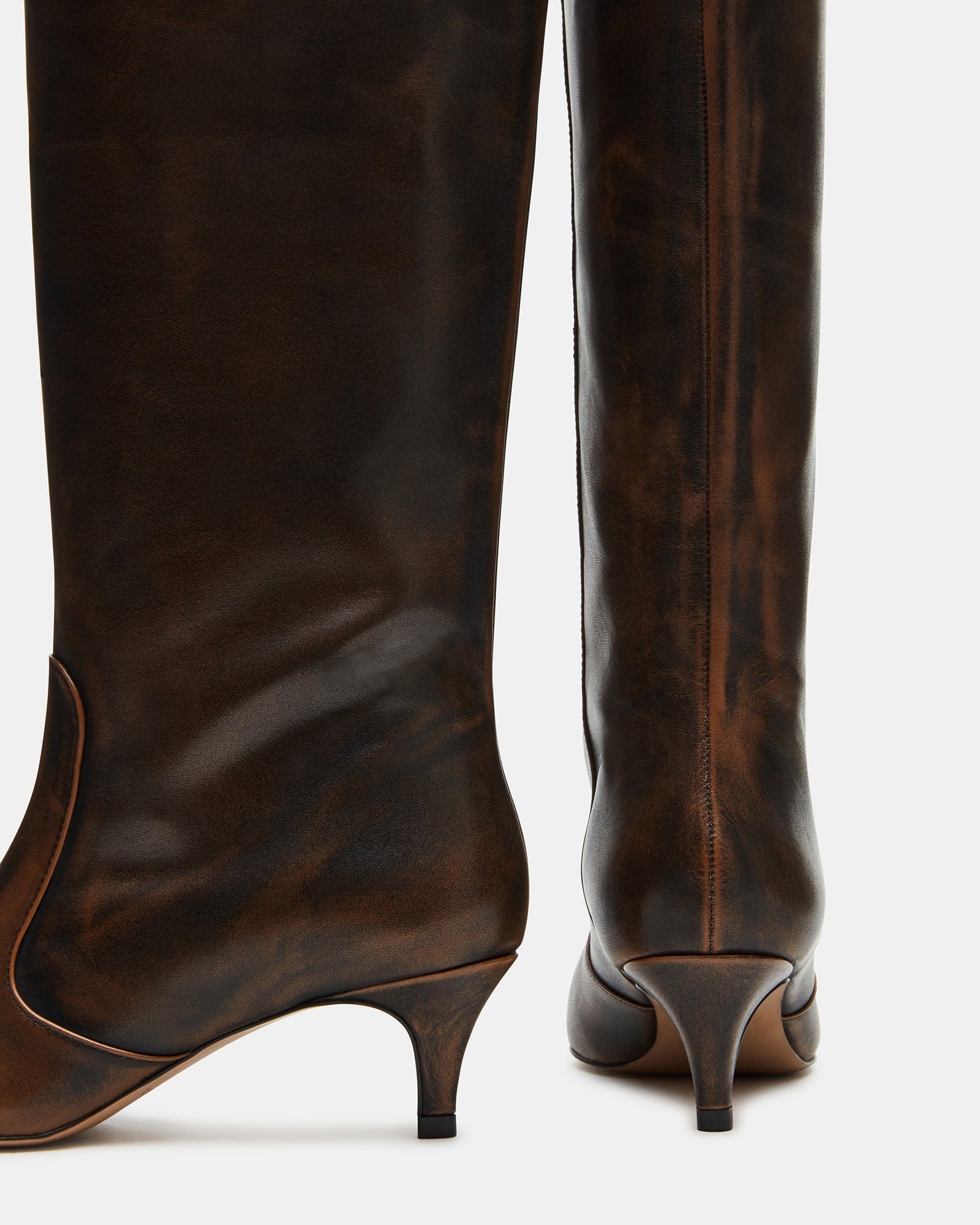 Side view of distressed brown knee-high boots with kitten heel, styled with jeans