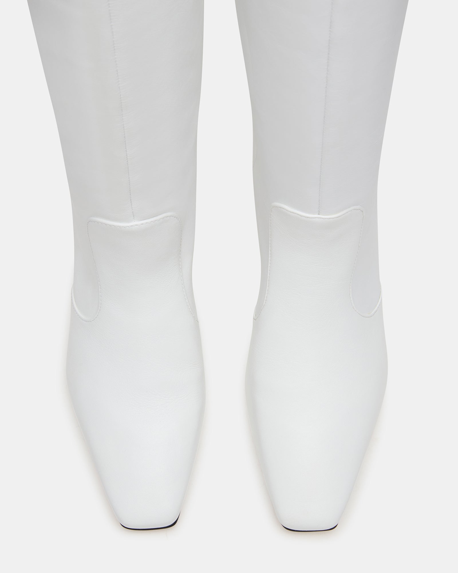 Full side profile of white leather knee-high boots on model in urban setting.