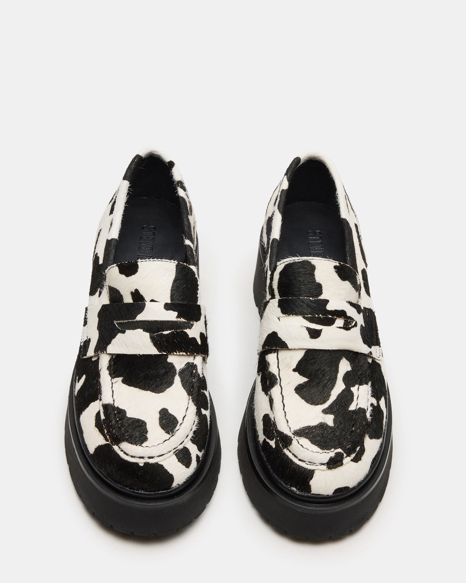 Side view of black platform loafers with cow-print detail, highlighting lug sole